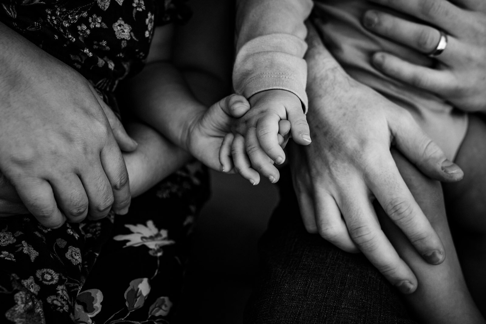 close up of young siblings holding hands with their parents' hands close by