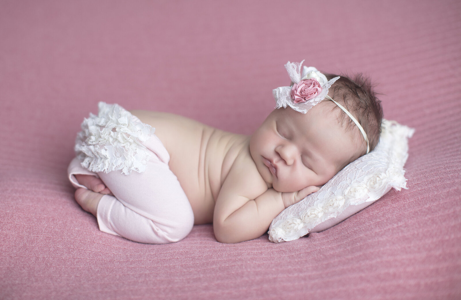 Newborn girl curled on pink fabric.