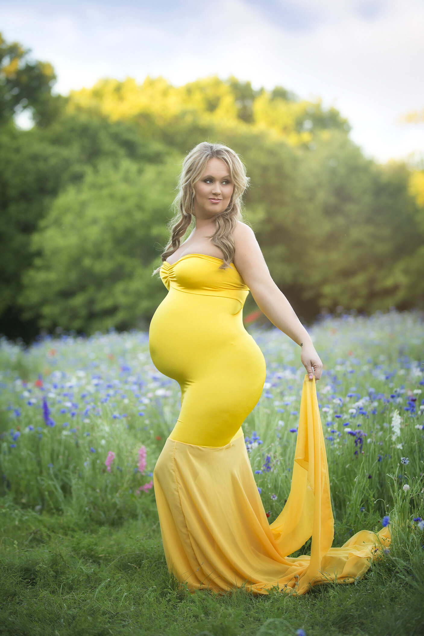 Pregnant woman with yellow maternity gown in wildflowers.