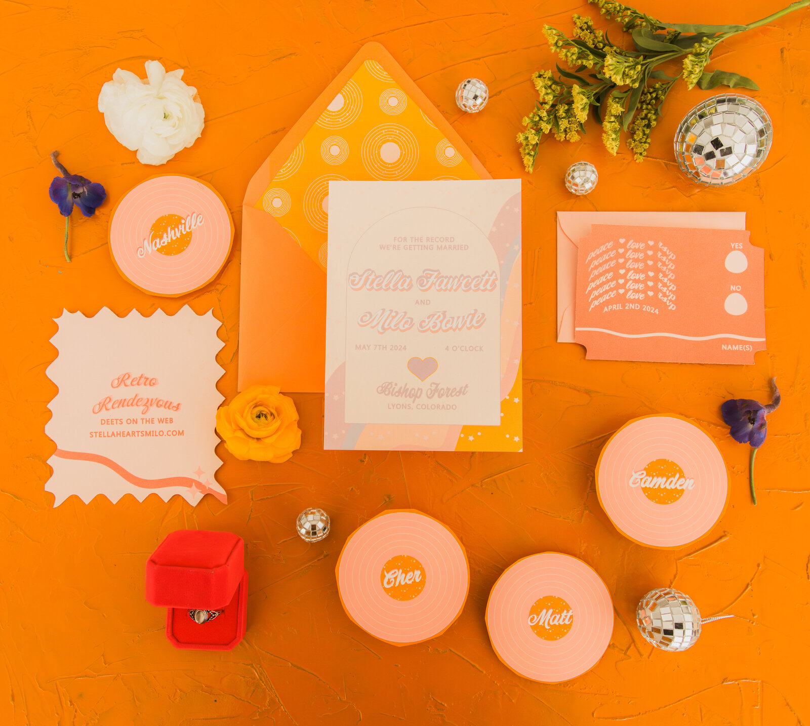 A retro themed wedding invitation flat lay with record shped wedding place cards, disco balls and flowers.