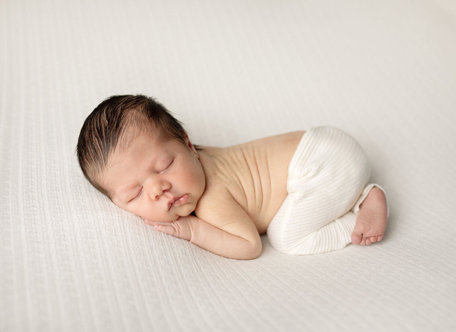 newborn baby boy posed on white fabric for newborn portraits 