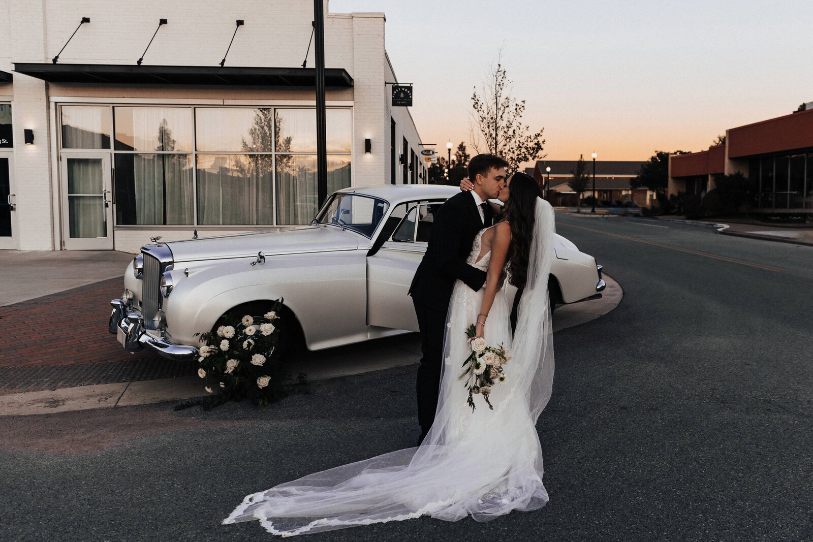 Tulsa Wedding Photographer. Old fashioned love. A bride and groom share a kiss in front of a vintage car with the beautiful sunset behind them. 