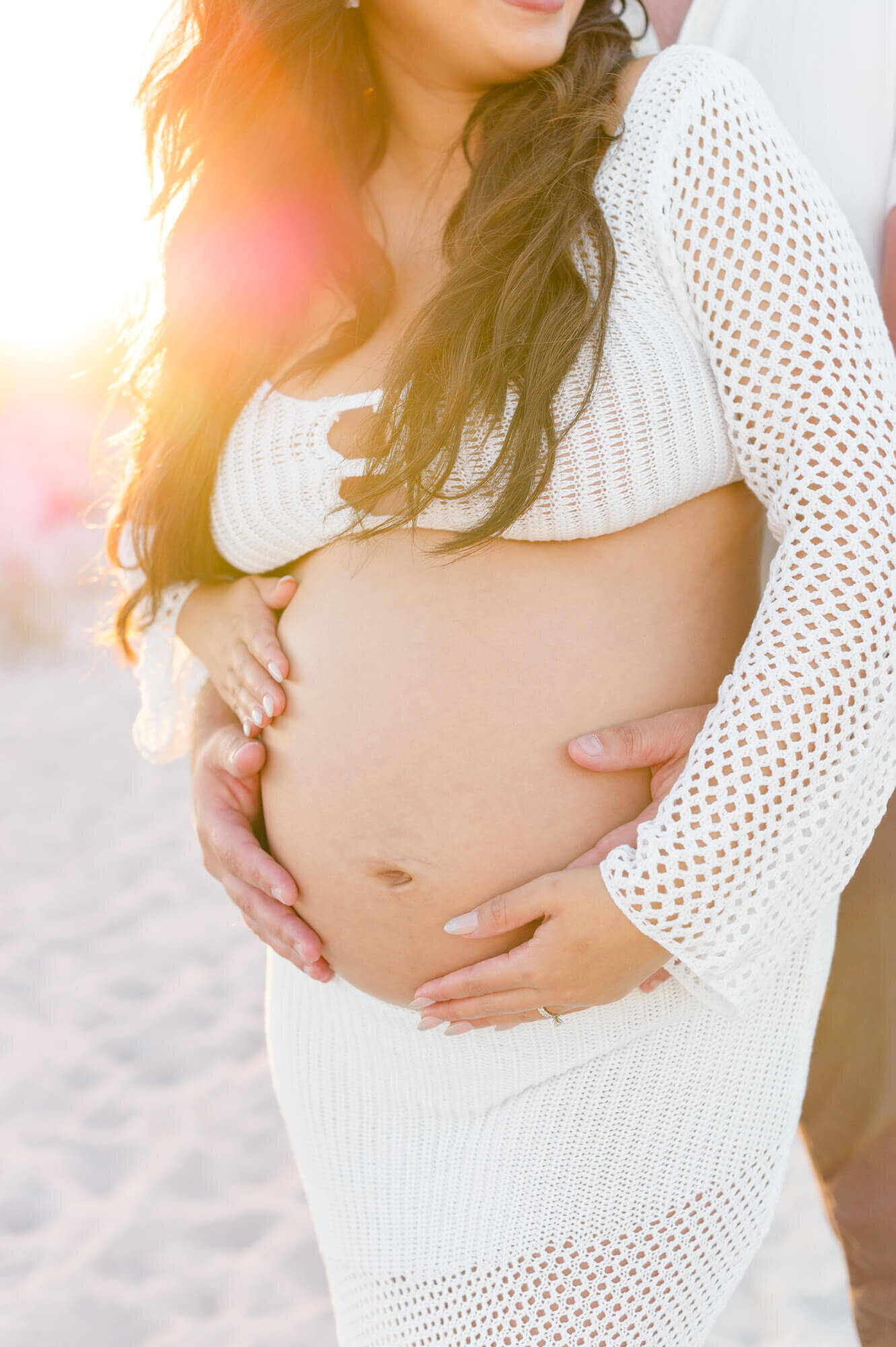 A close up image of the mothers belly with a beautiful golden hour glow behind her to the  right