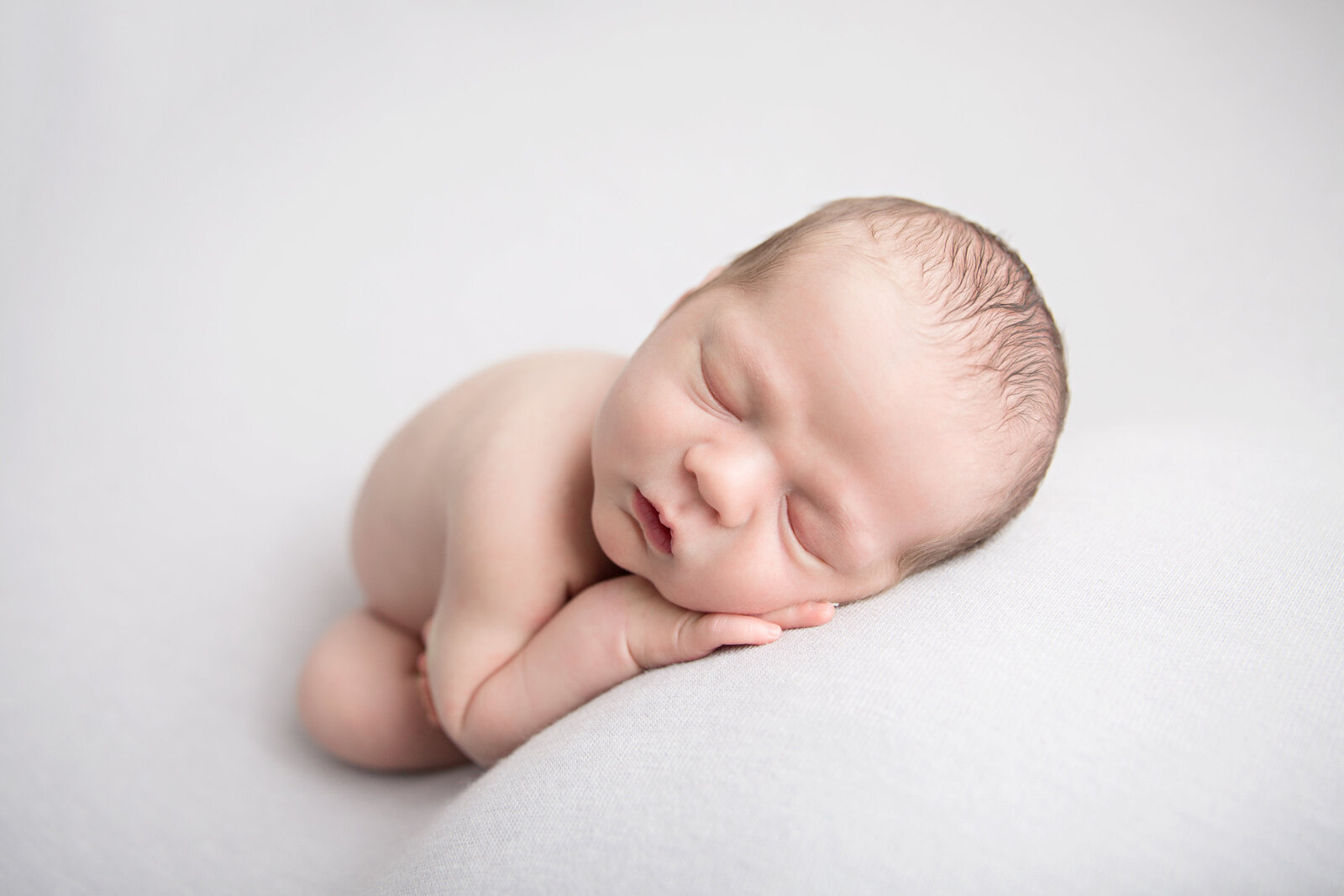 newborn baby laying in womb pose on light grey fabric