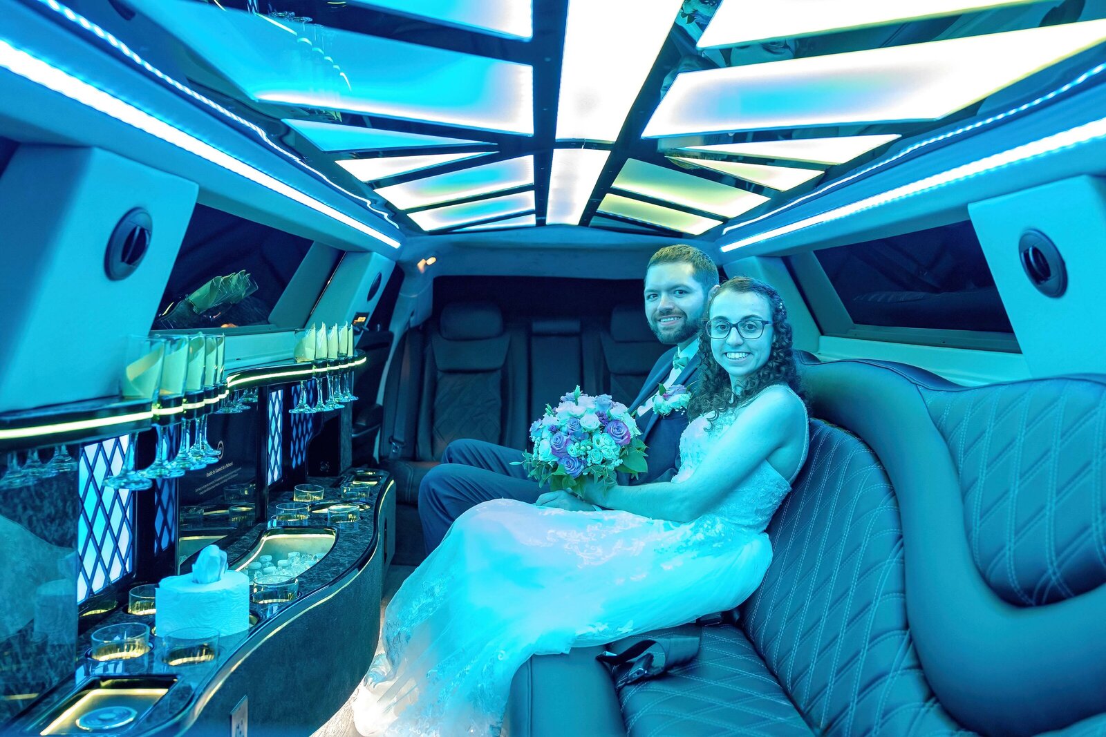 The bride and groom sit together in a luxury limousine with glowing blue lights and champagne flutes, captured during a Asheville, NC wedding, blending modern elegance with celebratory charm.