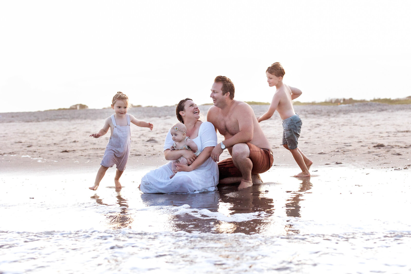 Two young boys running around their parents and baby sister at the edge of the water on the beach in Ocean City, New Jersey