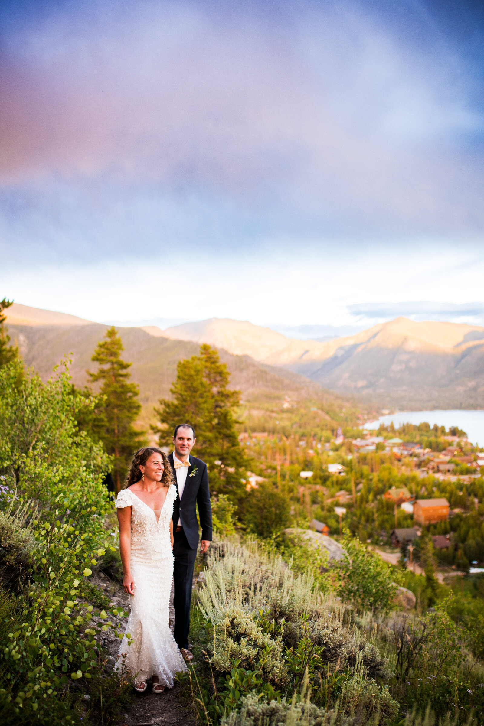 Bride and groom walk hand-in-hand toward the camera at golden hour with a Colorado mountain landscape in the background.