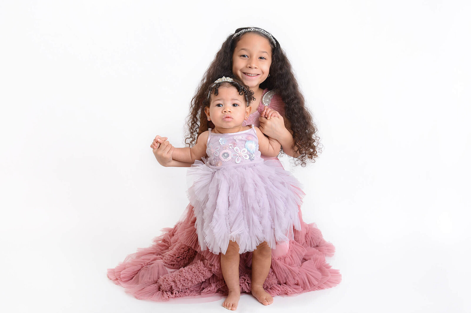 big sister cuddles up to her baby sister at their photoshoot