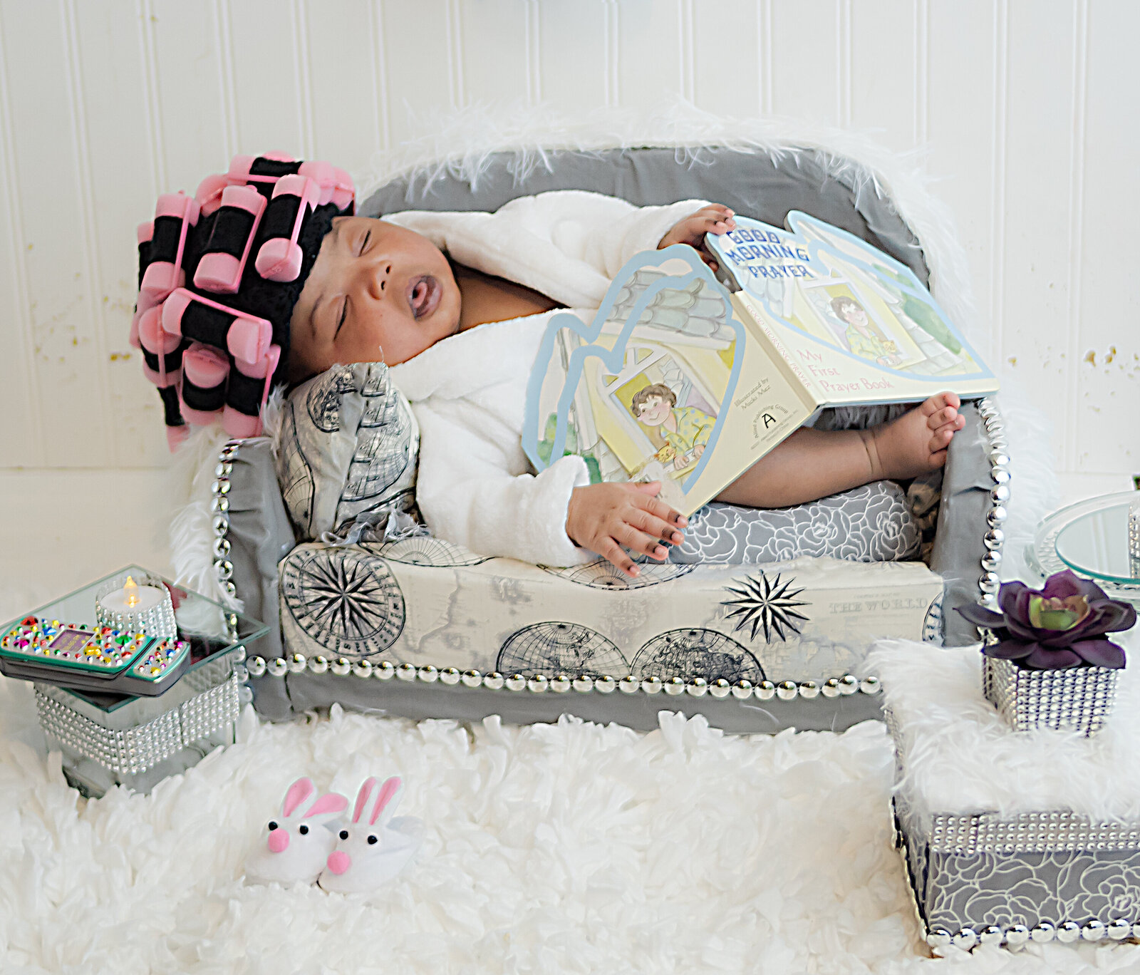 Newborn in dressed in robe with rollers laying on mini couch