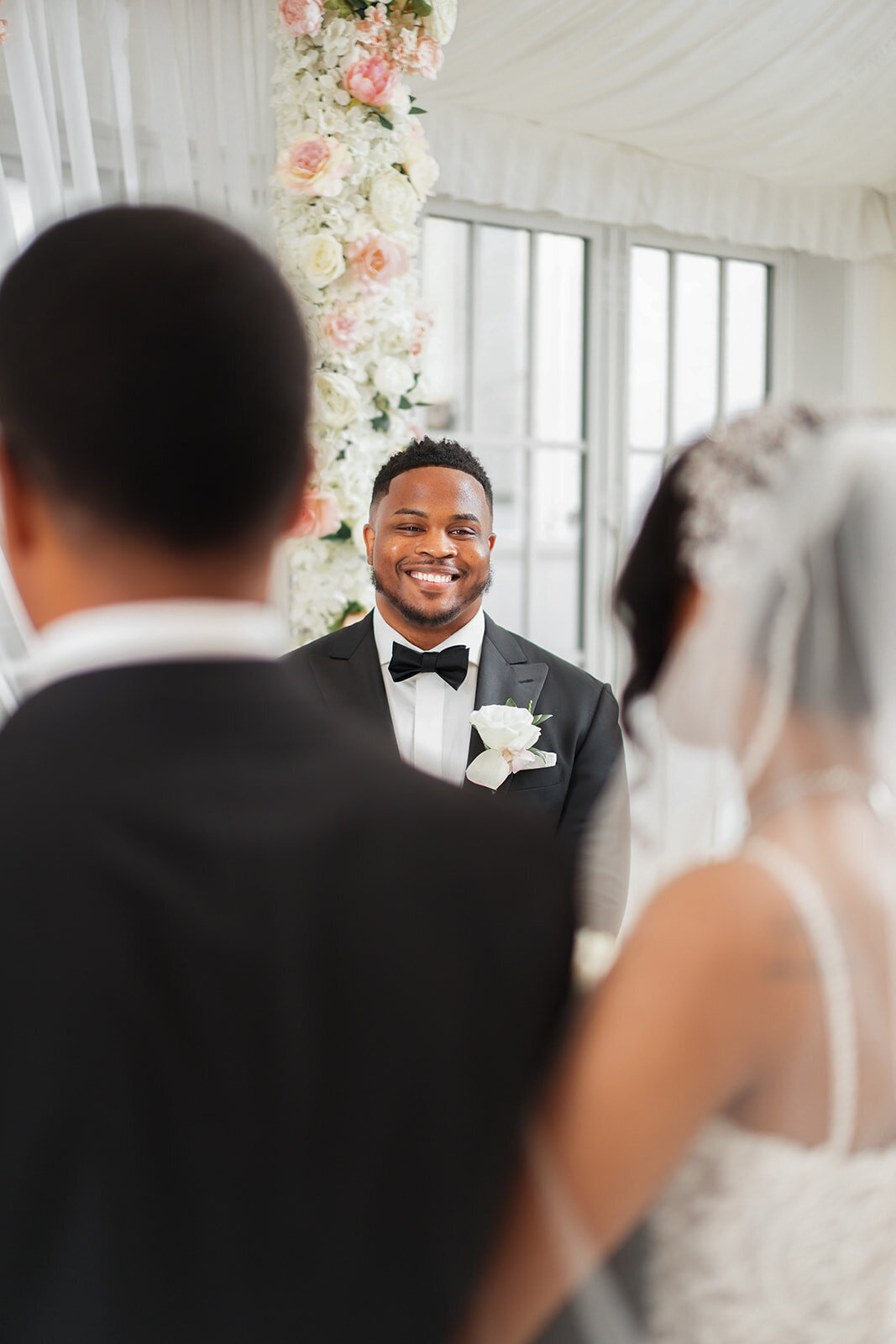 Groom smiling as bride walks down the aisle with her father