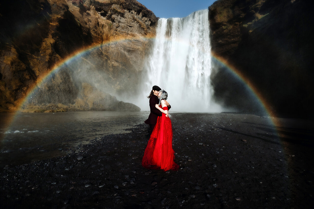 Newly weds are kissing in front of a waterfall in Iceland below a rainbow