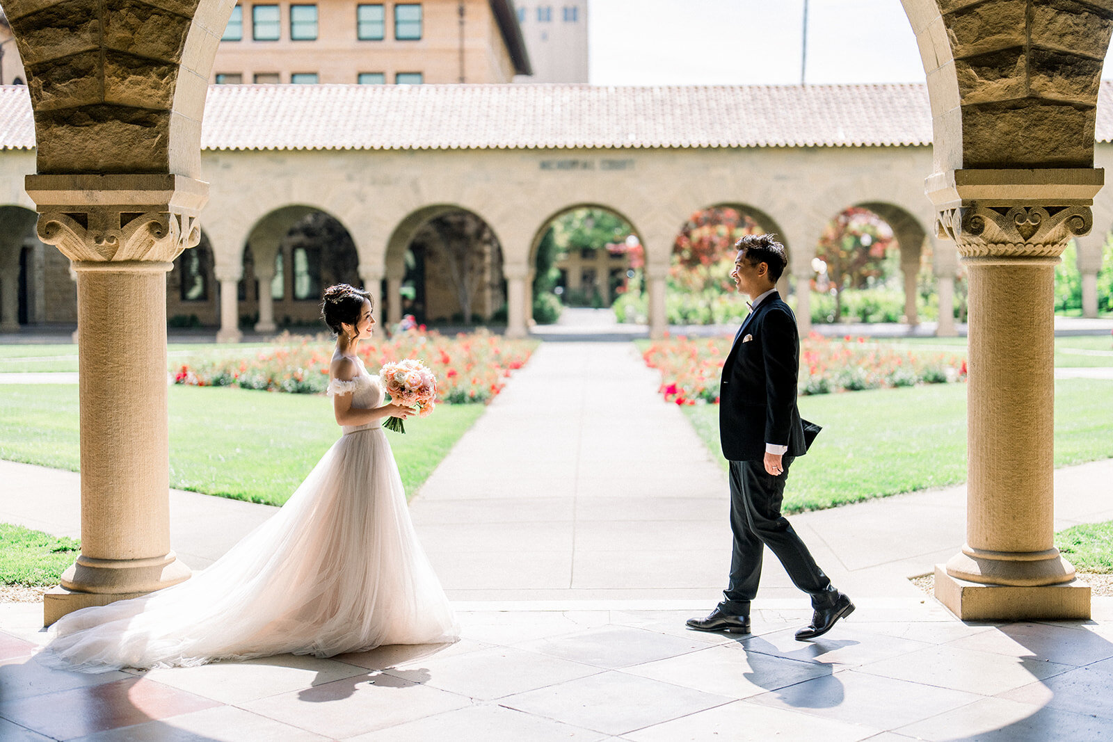 The bride and groom walk hand in hand, capturing a romantic moment at the iconic Stanford University.