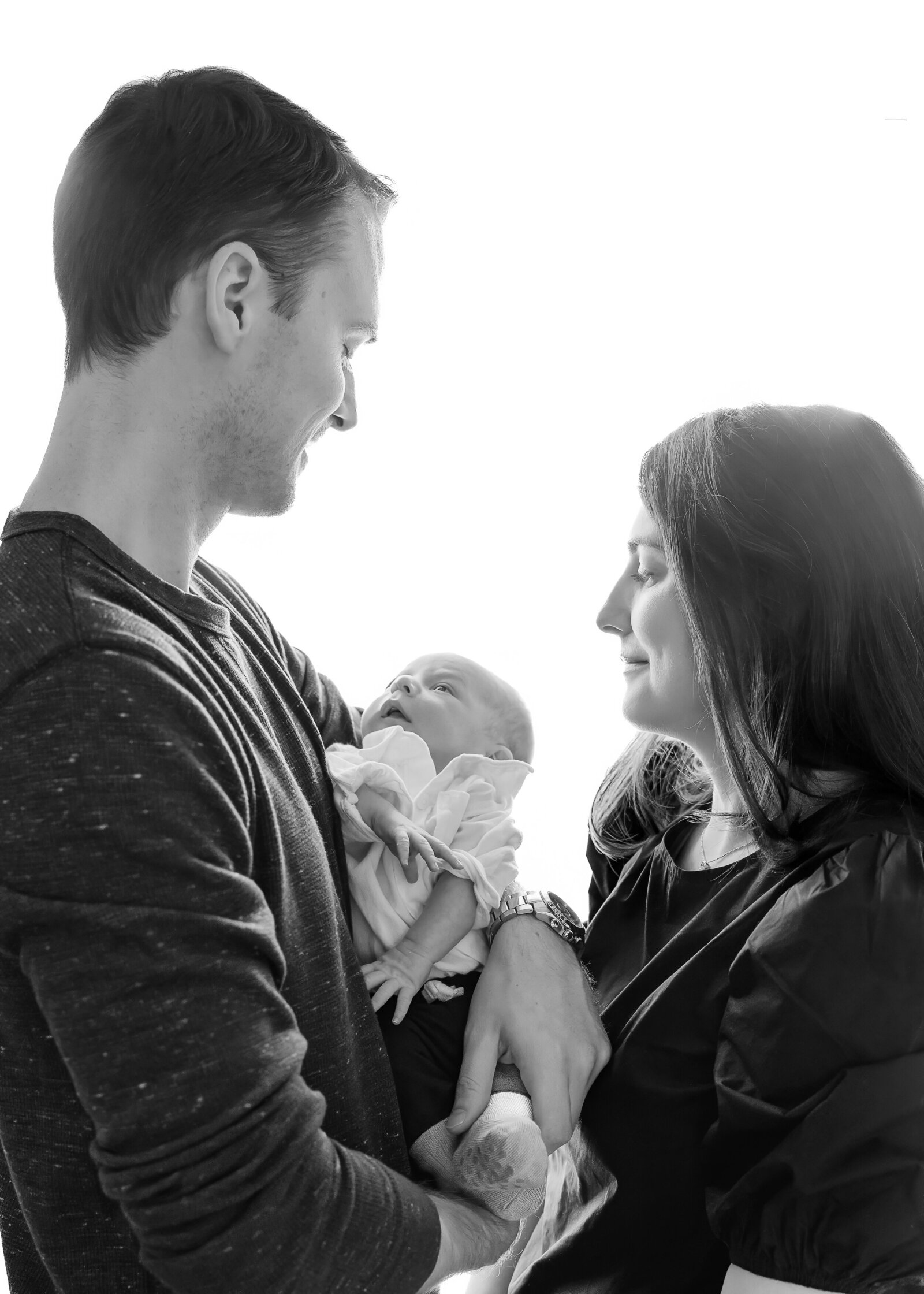 Backlit lifestyle portrait of family, featuring a newborn baby.