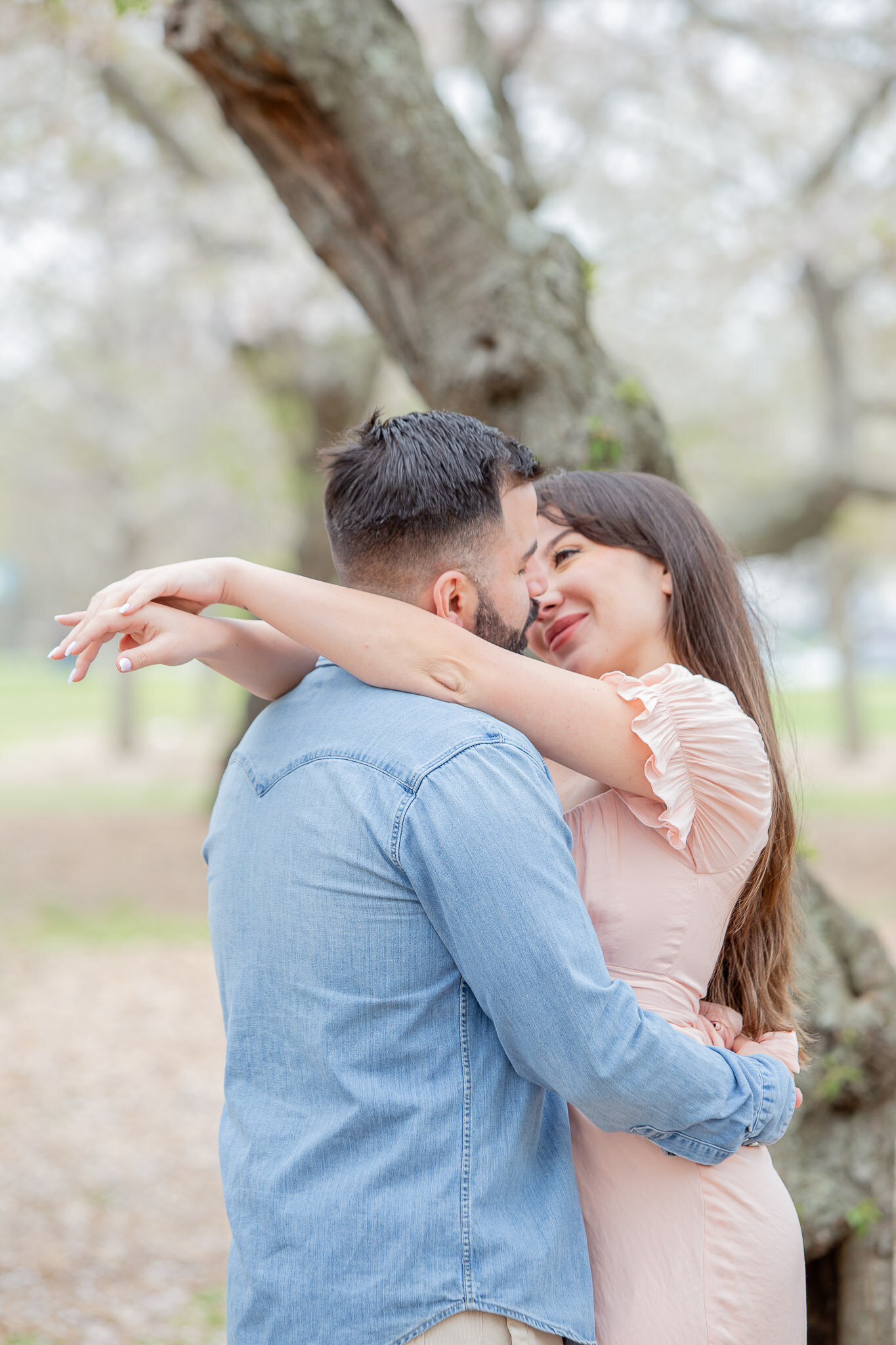 A woman is about to kiss her significant other in the middle of a grove of cherry blossom trees in Washington D.C.