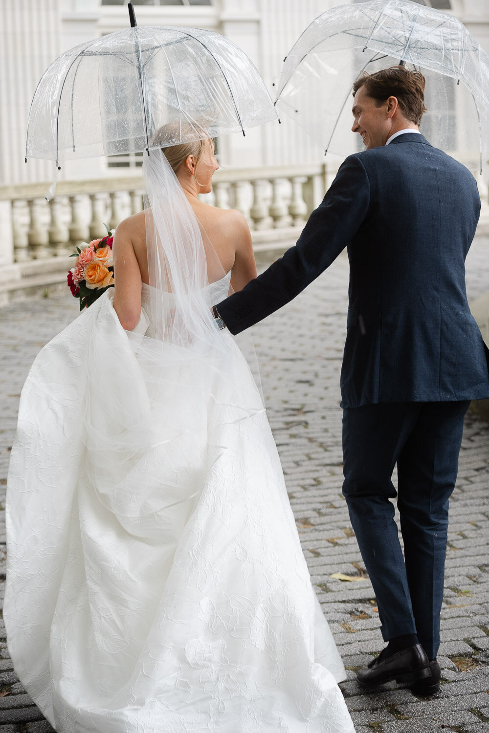 bride and groom walking from behind with umbrellas