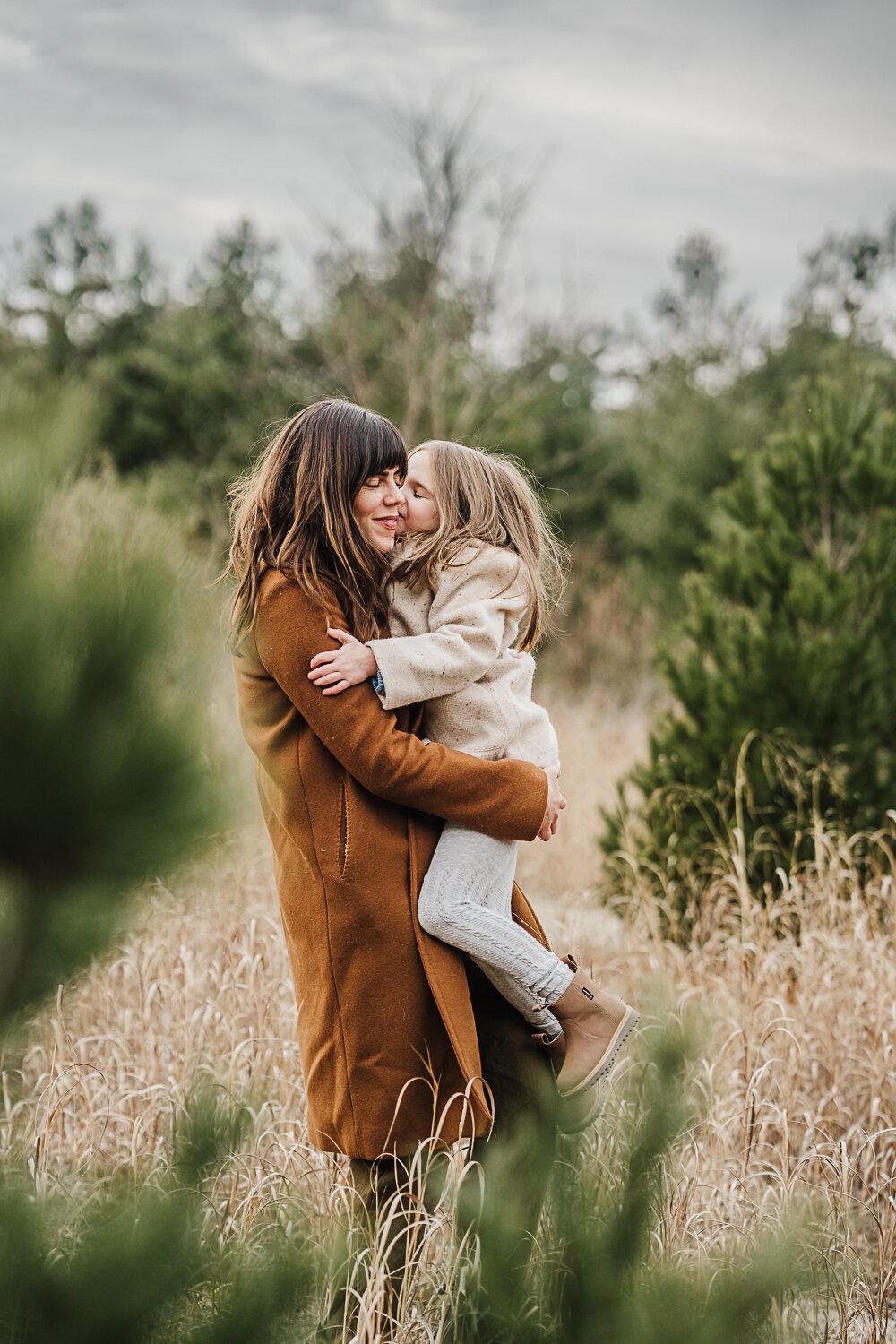 school aged girl hugs mom during family photos with evergreen trees