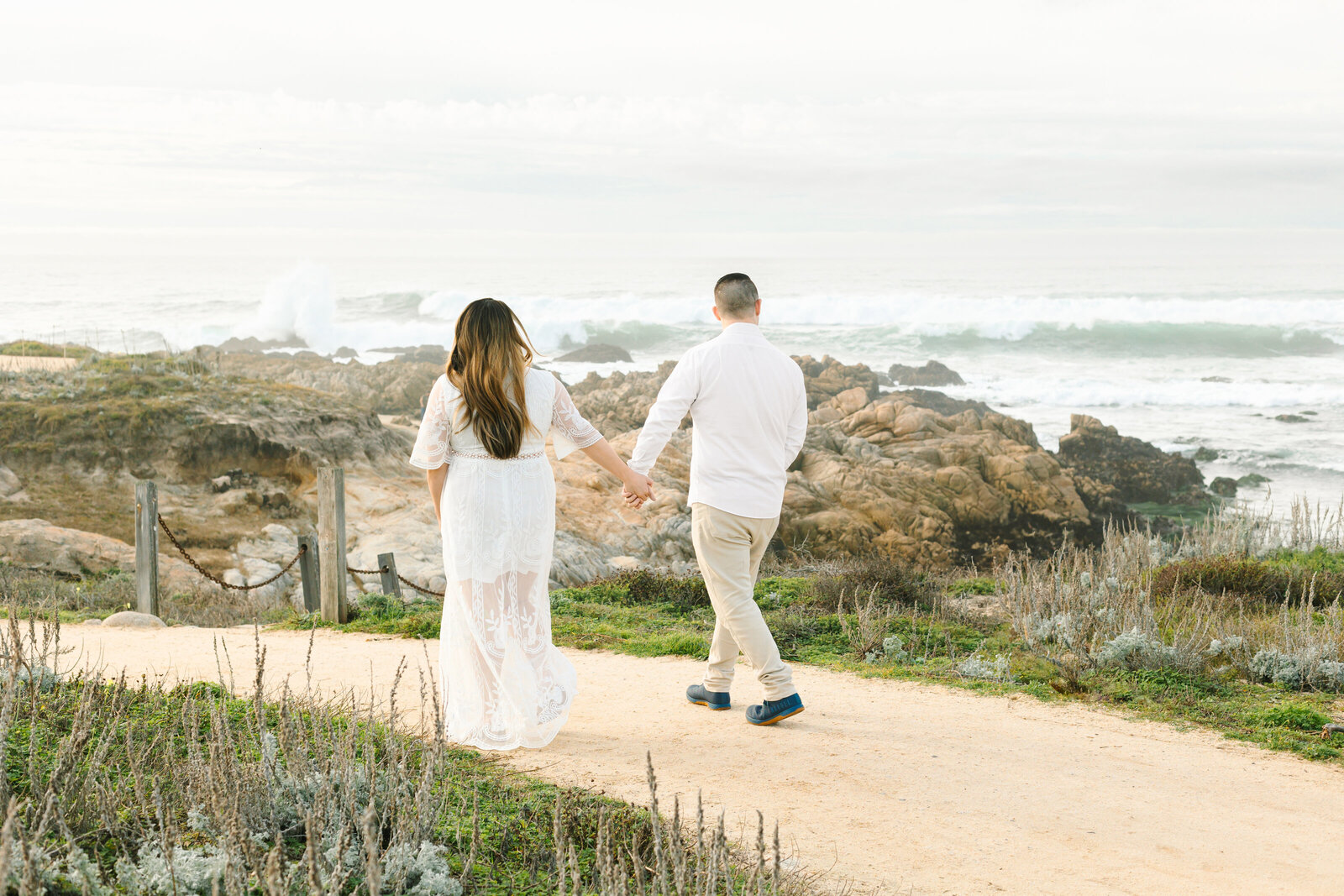 An engaged man and woman take photos on the beach in Pacific Grove, Monterey, California near Big Sur.