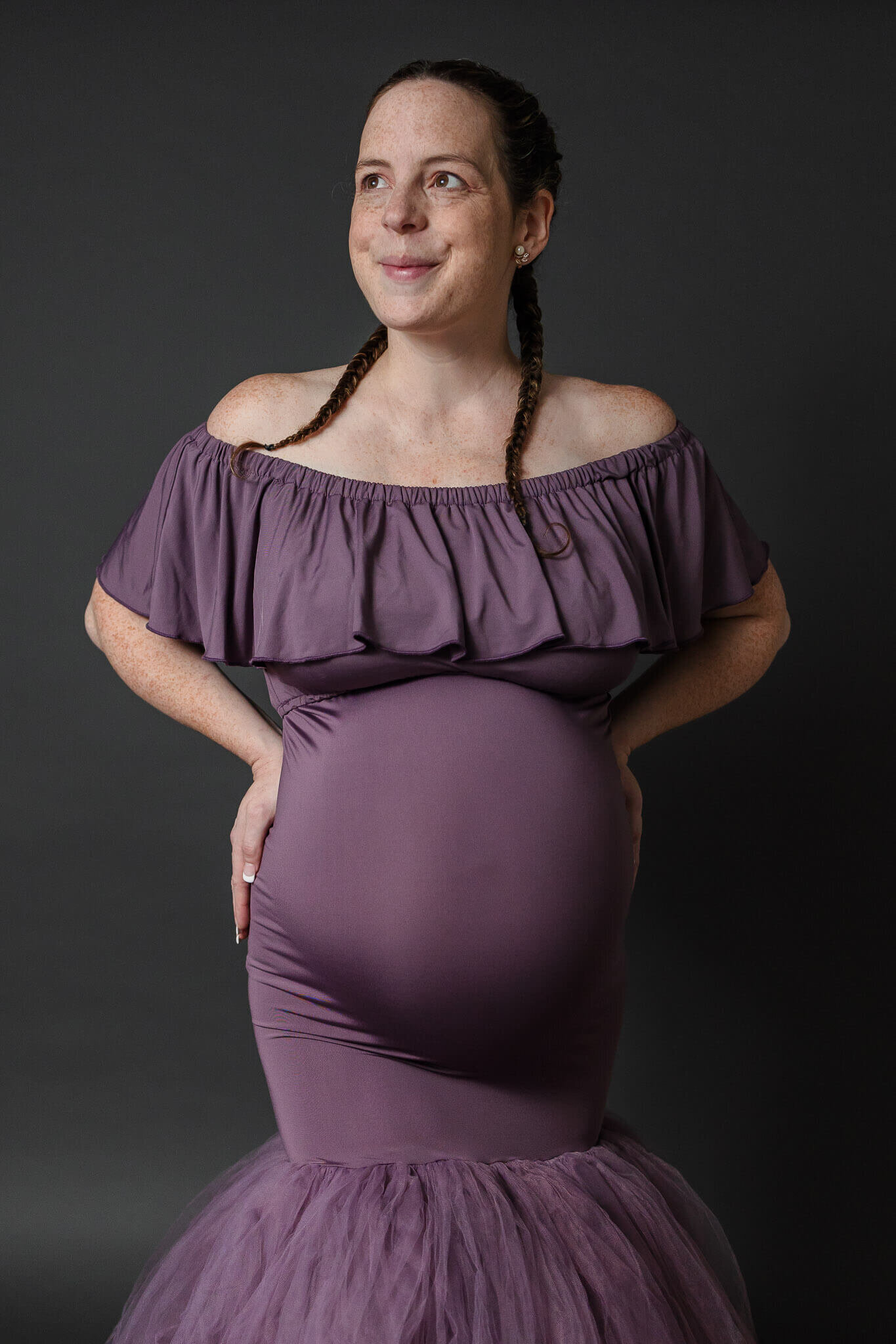 A mom-to-be in a purple dress posing in a Northern Virginia maternity studio.