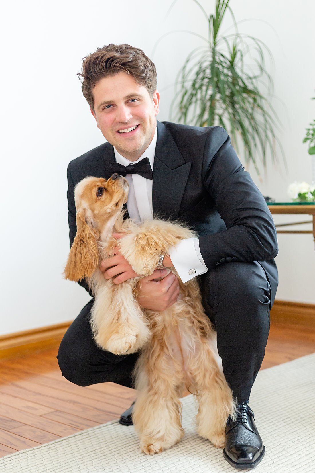 Handsome-groom-squats-down-to-hug-his-small-dog-on-his-wedding-day