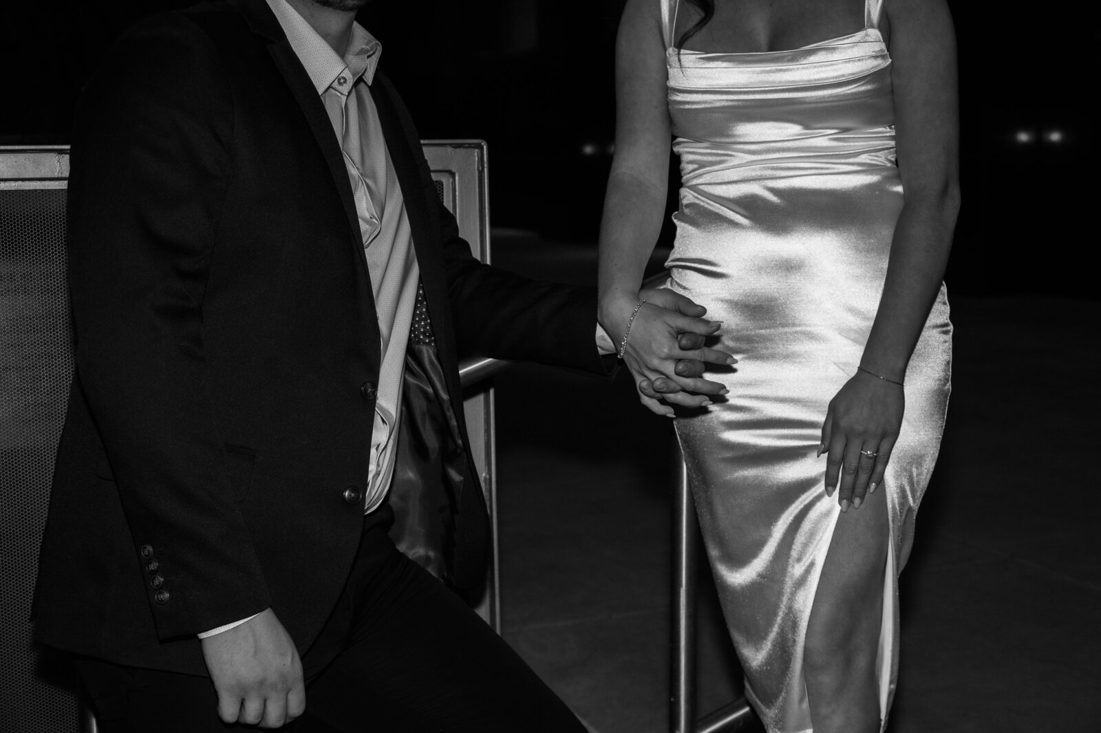 Black and white engagement portrait of a couple dressed in elegant formal attire, featuring the woman in a sleek satin dress, captured in a timeless and romantic photography style.