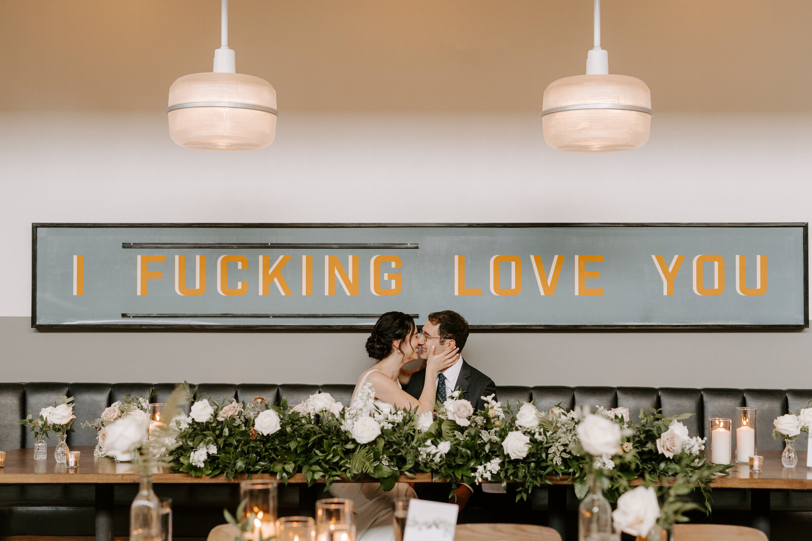 Couple embracing under sign that reads "I fucking love you" at Olive and Oak wedding venue in Webster Groves, MO