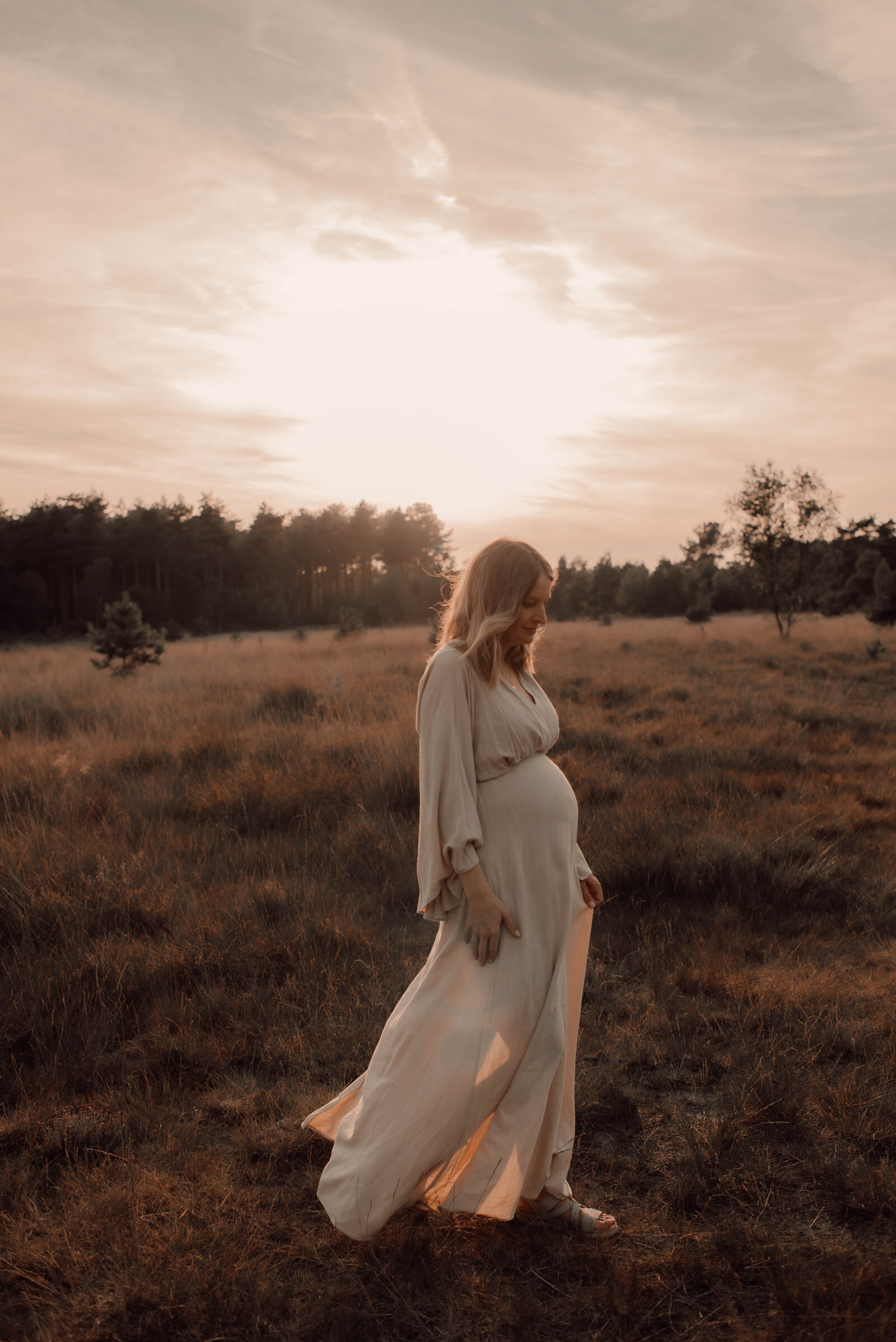 Zwangere vrouw in jurk poseert voor zwangerschapsshoot tijdens zonsondergang op de Kalmthoutse Heide