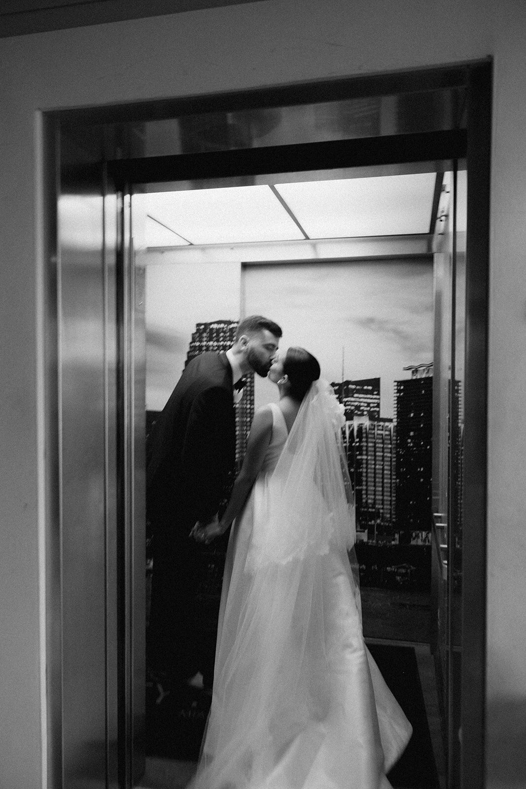 Newlywed couple kissing in the elevator featuring a skyline background in black and white | Sush Digital Media
