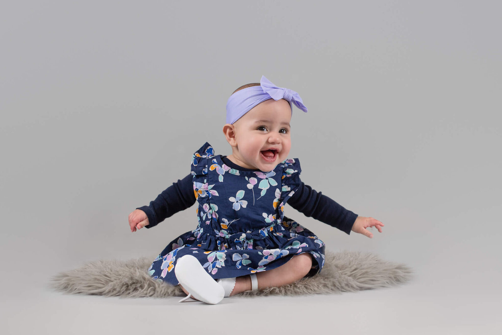 Six month sitter session of baby girl in floral navy dress smiling at camera in studio on gray background