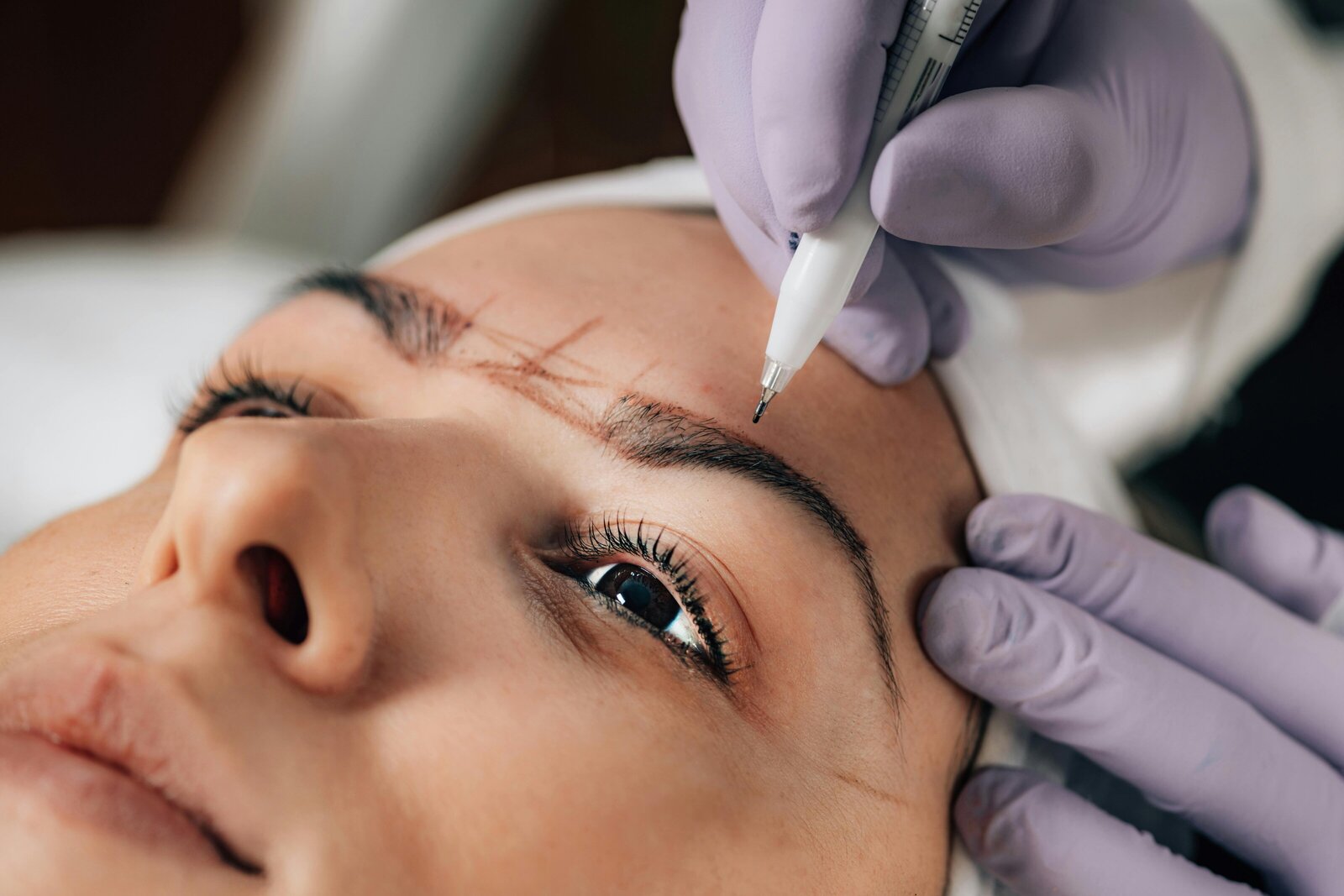 A permanent makeup artist shaping a client's eyebrow with a microblading tool