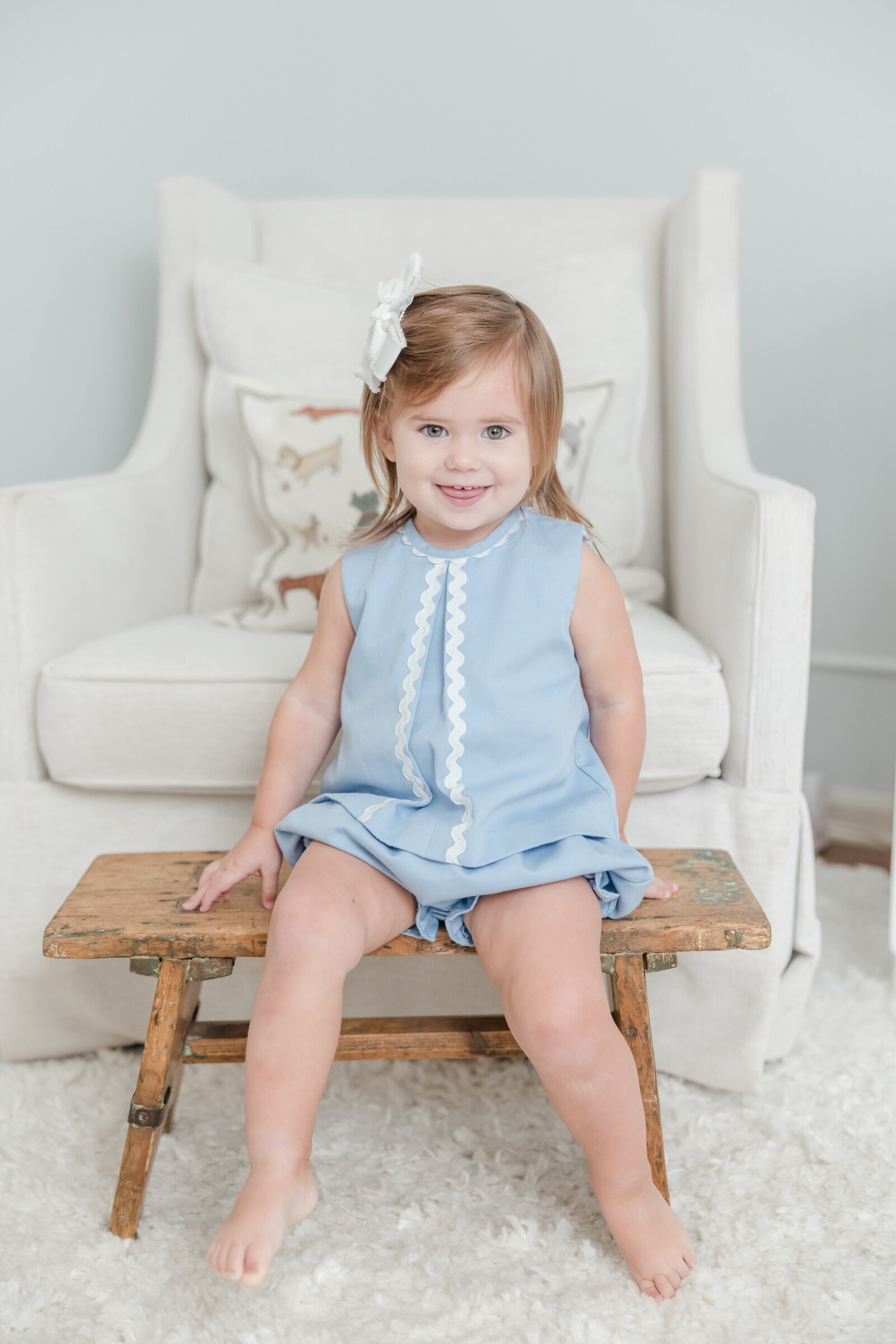 Portrait of a toddler girl sitting on a wooden stool and smiling.