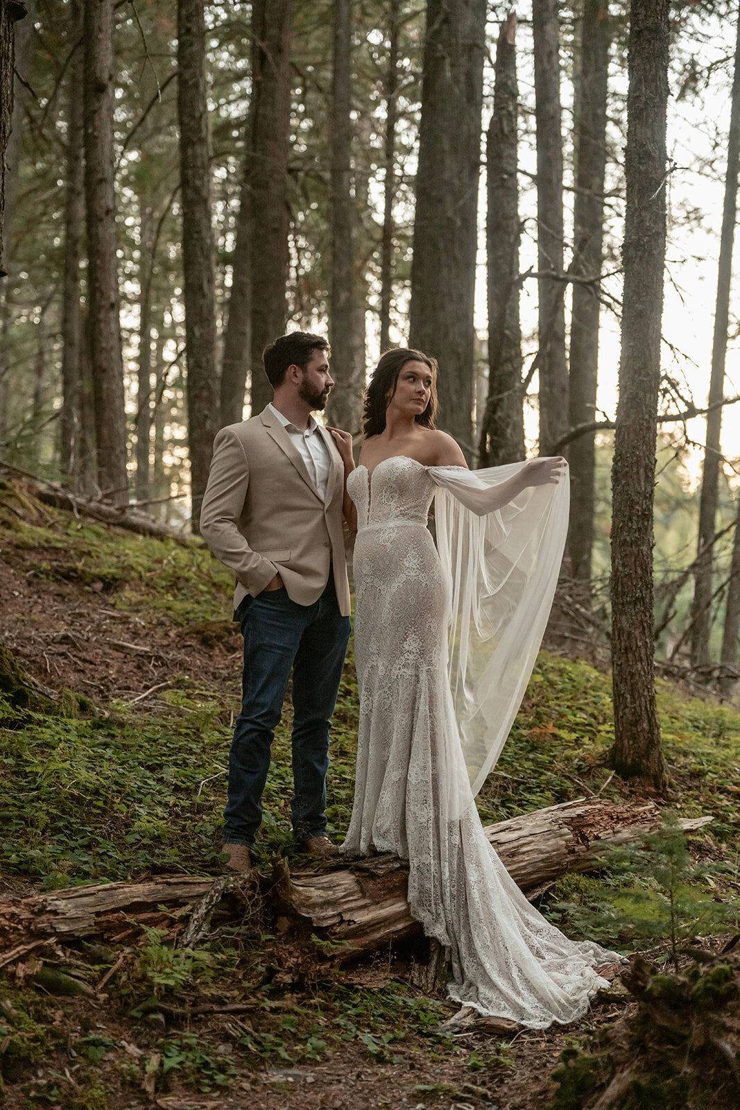 A bride and groom stand together in a forest surrounded by soft evening light filtering through the trees during their Glacier National Park elopement, captured by Sydney Breann Photography.