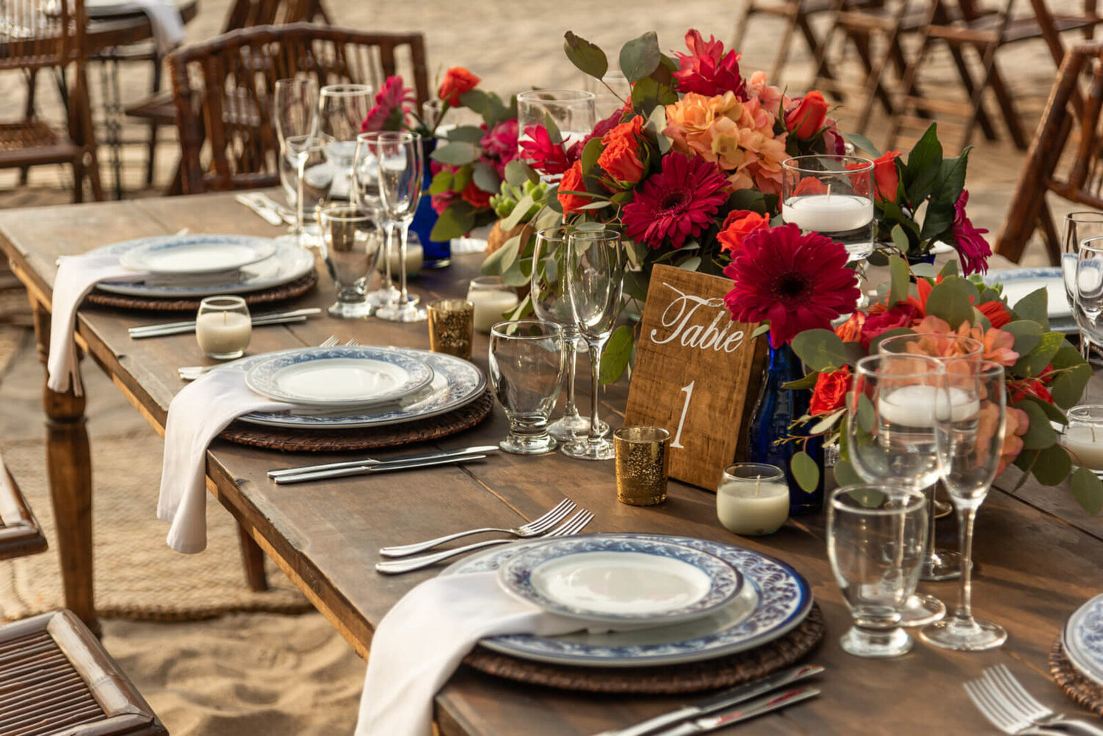 Luxurious wedding dining table with plates, glasses and colorful floral centerpiece by the beach