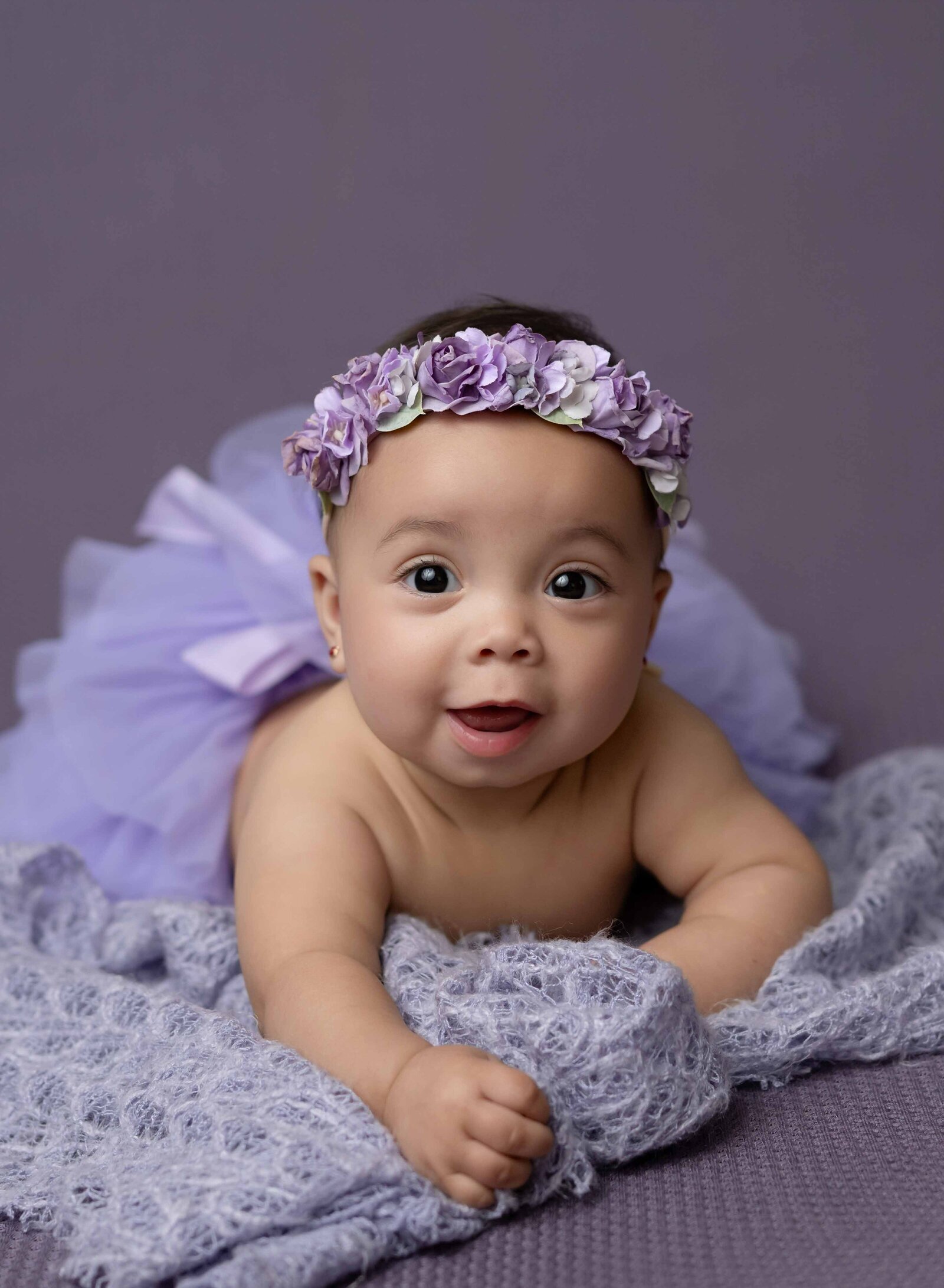 Baby girl in purple tutu laying on her belly with big open eyes. Photographed by Atlanta baby photographer.
