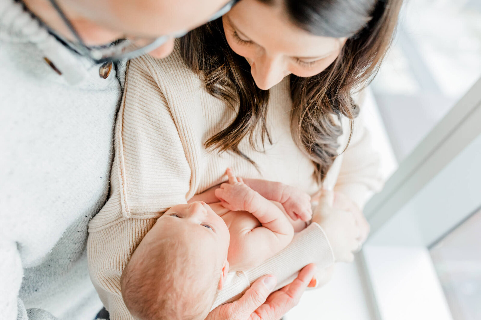 Taken from above, mom and dad stand looking at their newborn as the baby looks up at his mom