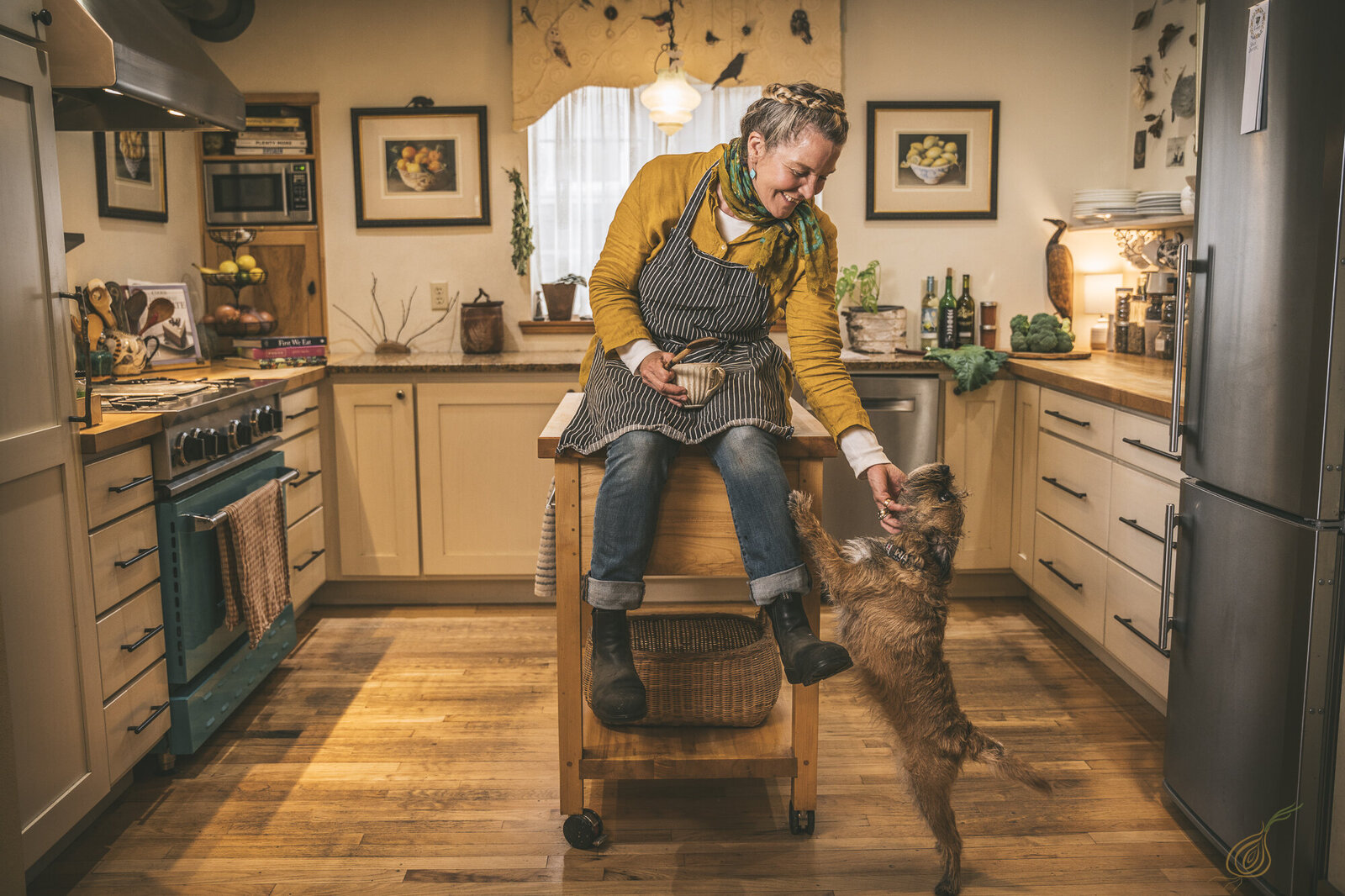 A woman sits on a kitchen island, smiling at her dog, creating a warm and inviting home atmosphere.