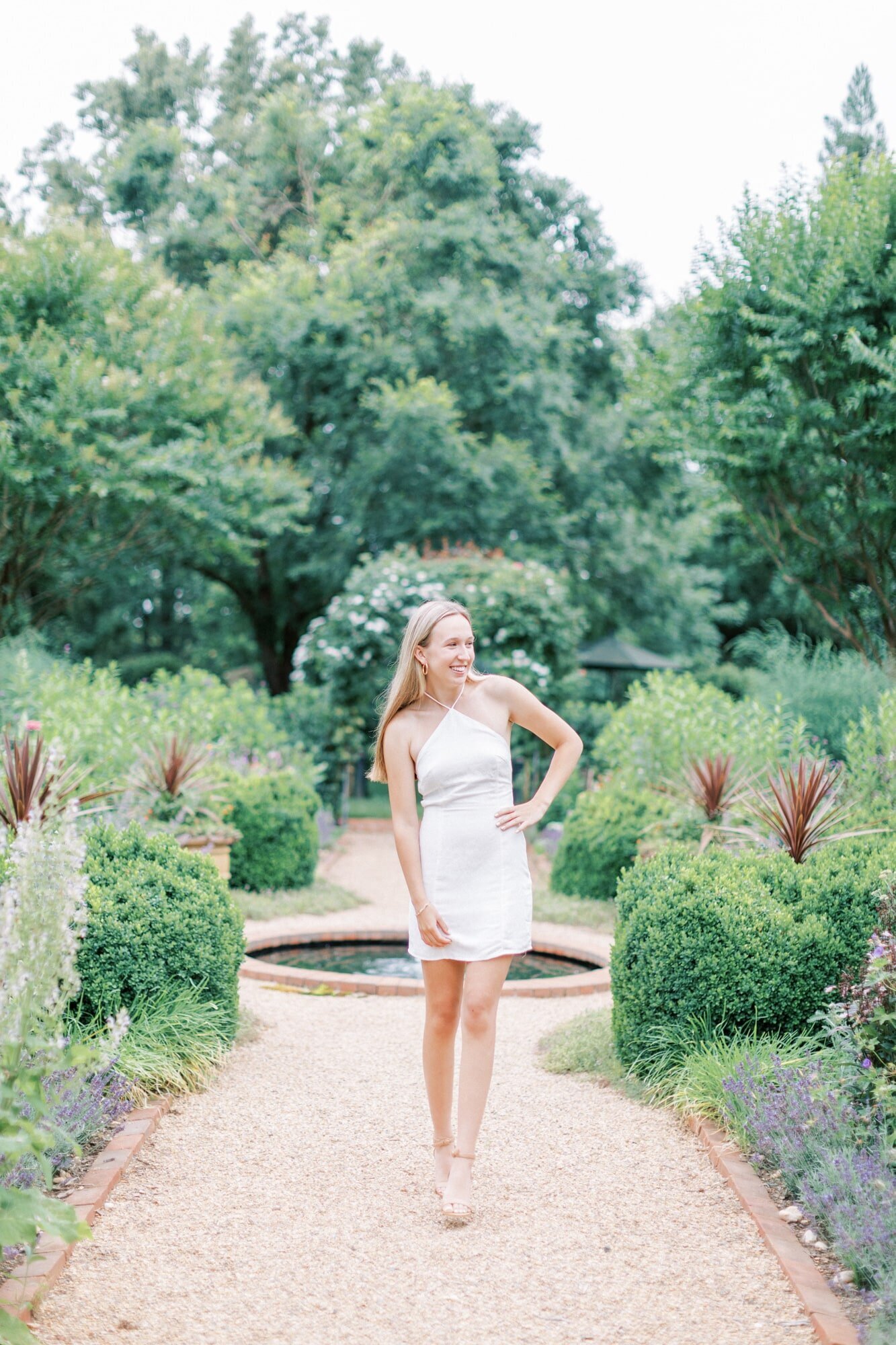 A blonde highschooler is wearing a white dress for her senior photos, taken in a cute garden outside of Charlottesville.
