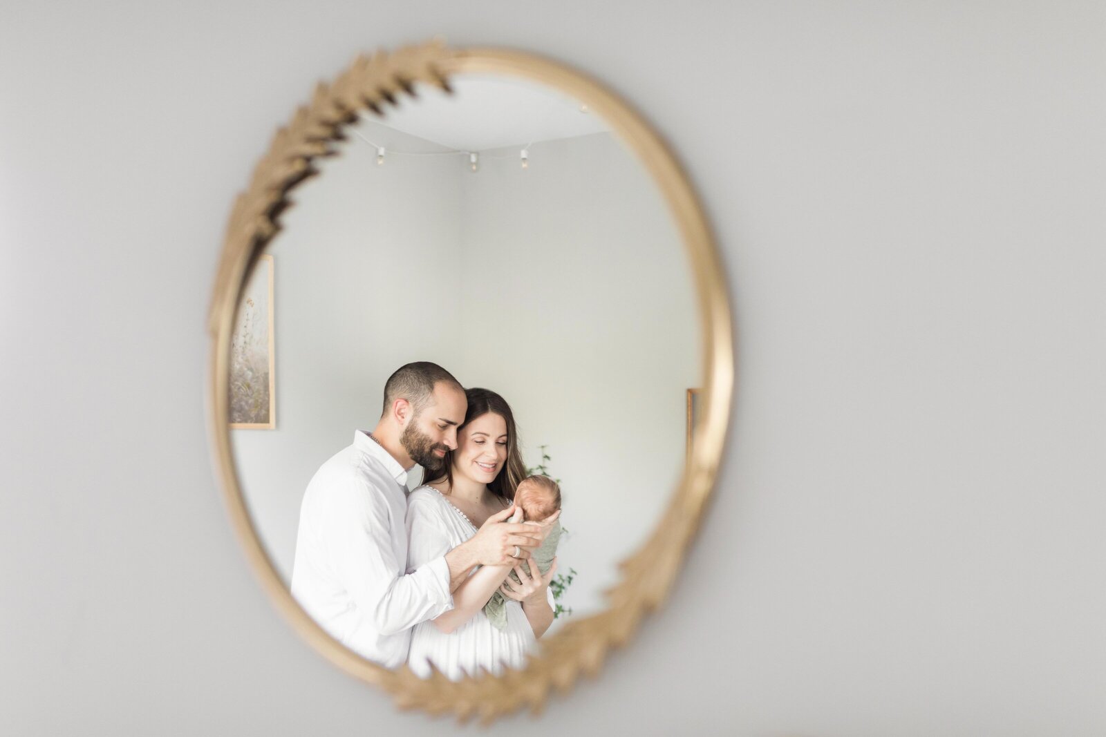 Northern Virginia Newborn Photography showing parents cuddling baby in nursery framed in a mirror