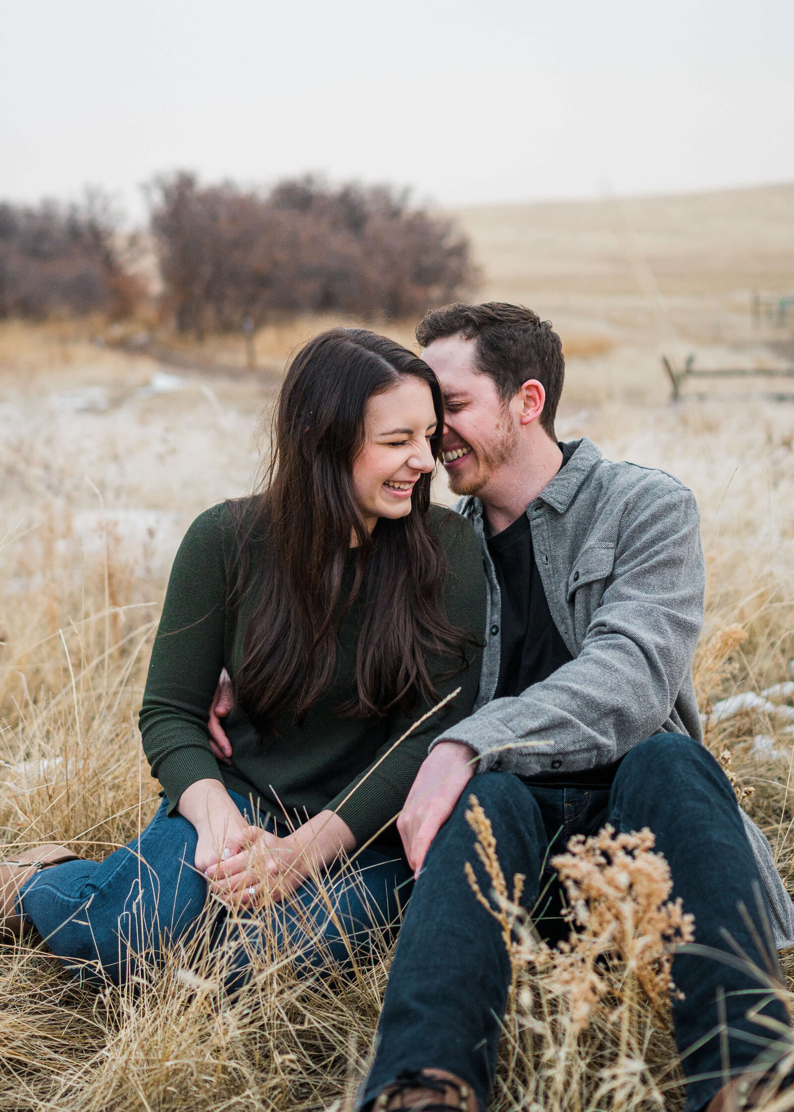 Woman and her fiance sitting in a field and laughing during engagement photo session