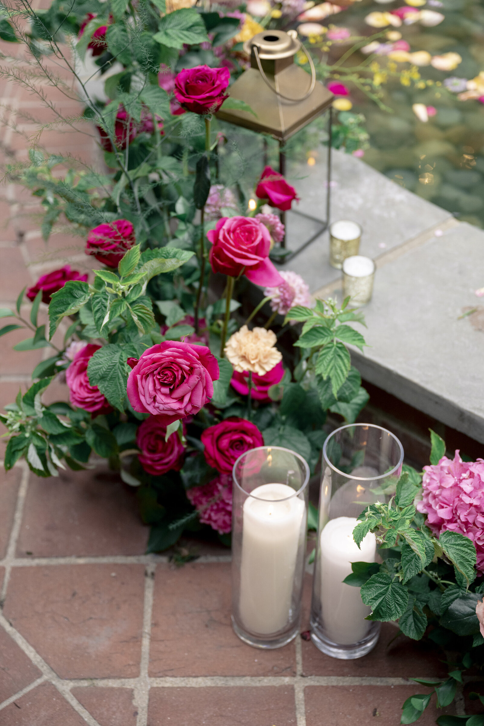 Close up of water fountain floral installation with hot pink roses, peach carnations, greenery and ivory pillar candles.