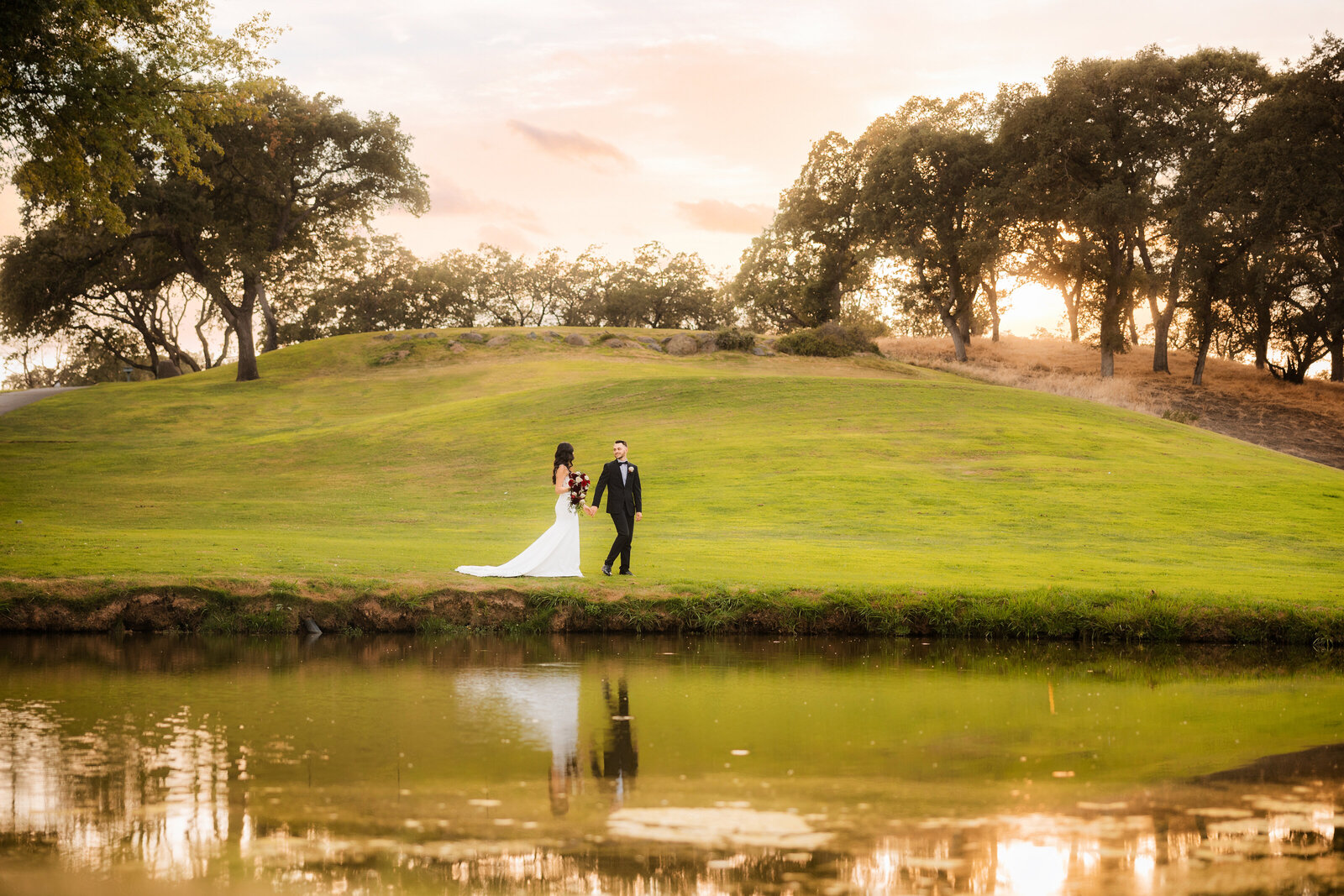 bride and groom walk in front of a pond after wedding ceremony. Groom looks back at bride as she follows him. Photo by Sacramento wedding photographer, Philippe Studio Pro.