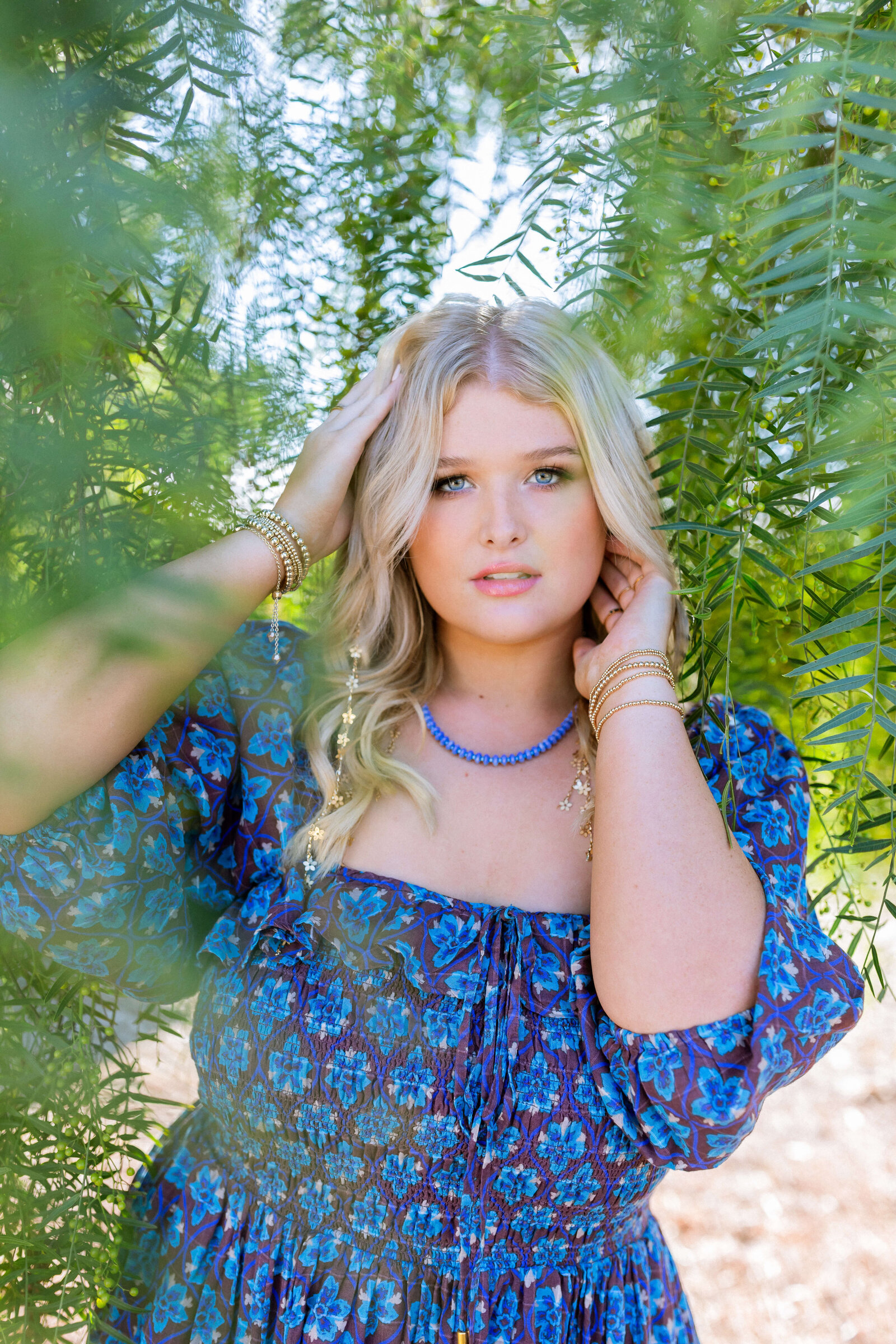 blonde girl wearing blue dress and posing under a tree