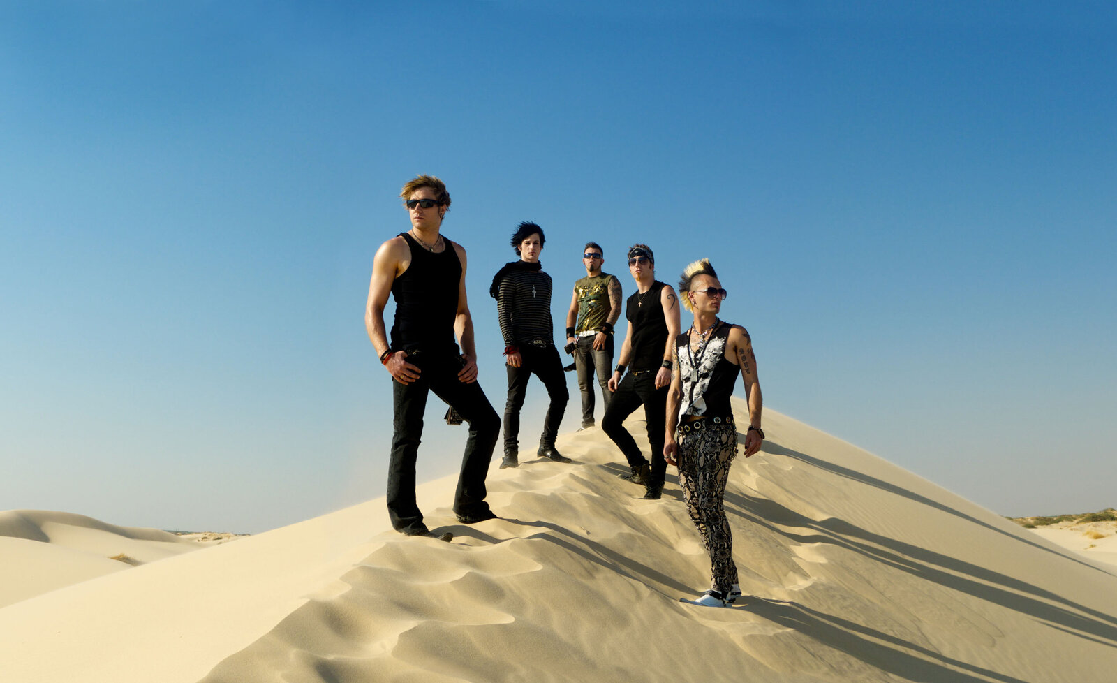 Music group portrait standing on sand hill blue sky background