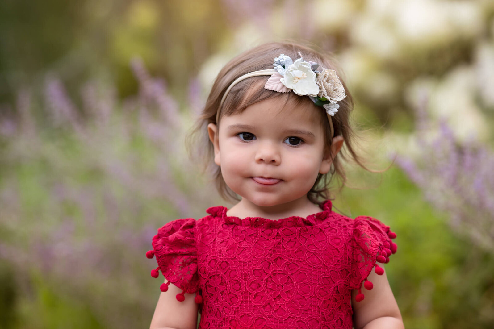 Little girl in red dress with floral headband sticking tongue out