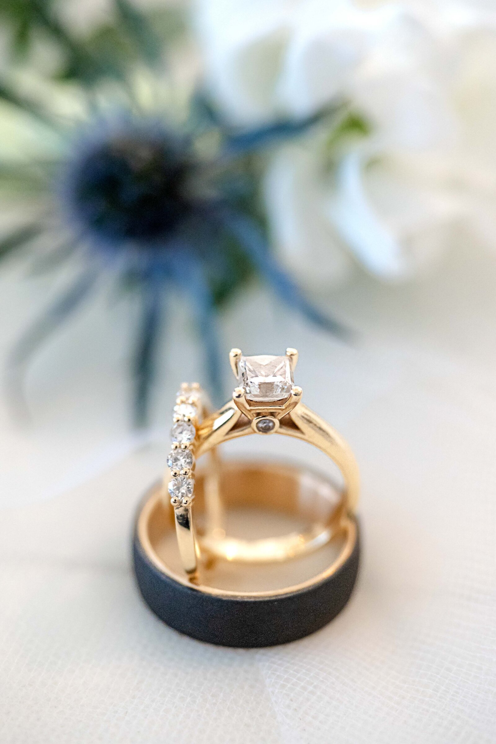 Close-up of gold wedding rings with a diamond engagement ring and floral background, captured at a Wilmington, NC wedding, highlighting elegant wedding details and timeless design.