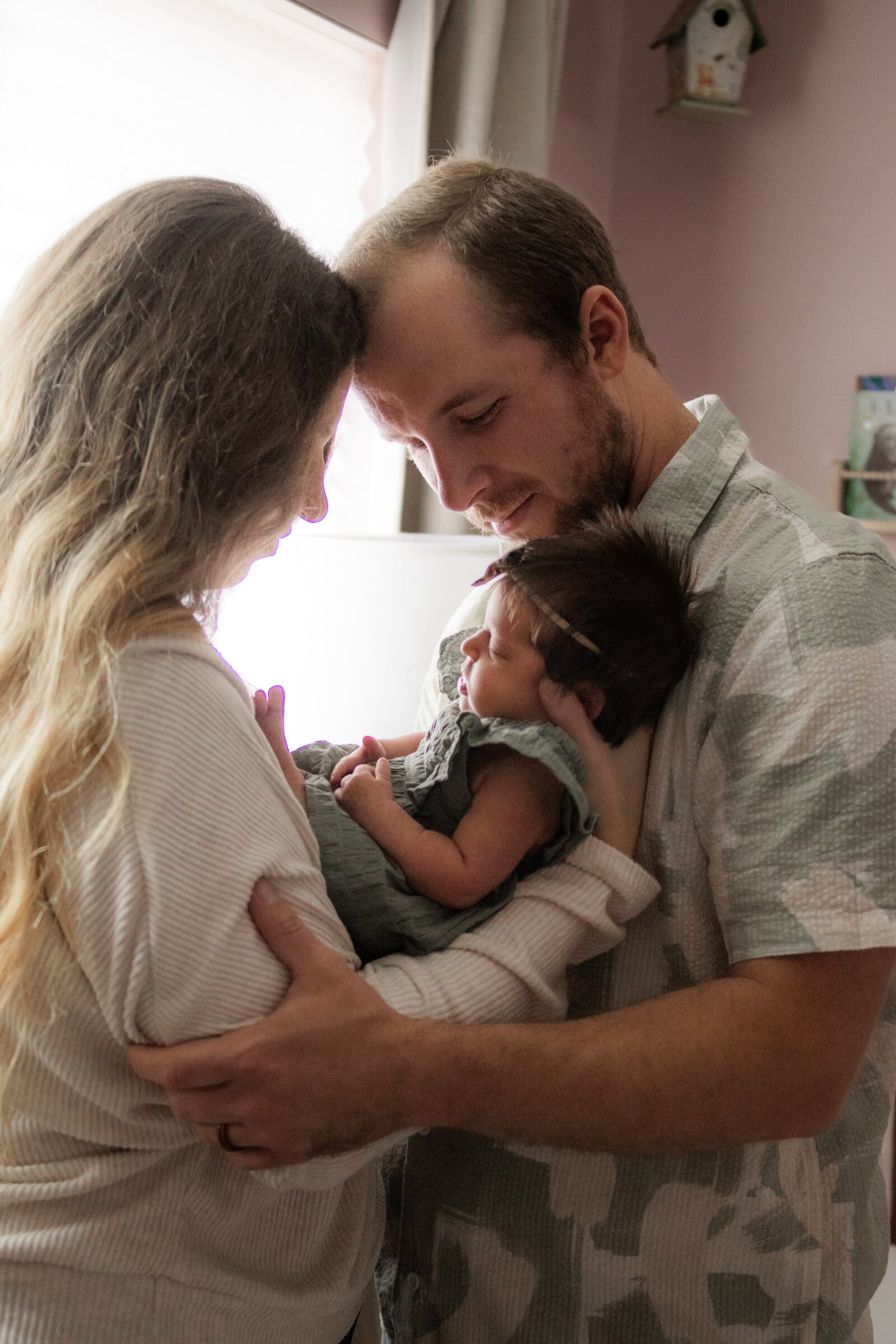 Mom and dad lovingly look down at sleeping baby girl cradled between them