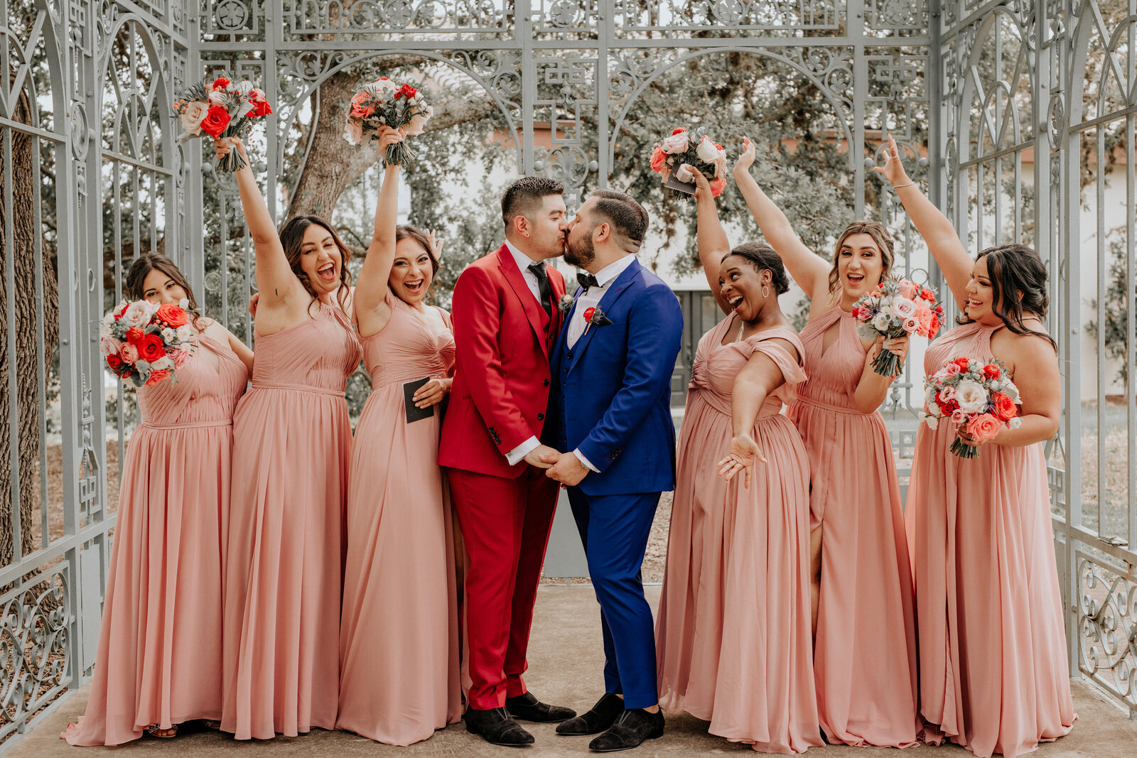 two grooms kissing surrounded by bridesmaids