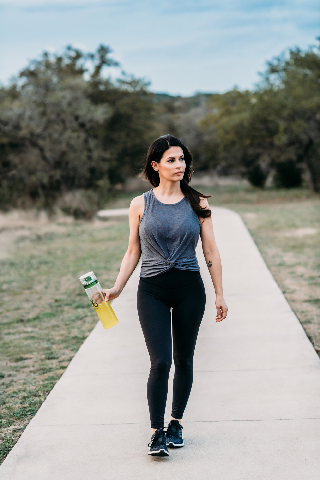Branding Photographer, a woman in fitness apparel  holds water bottle and walks on trail
