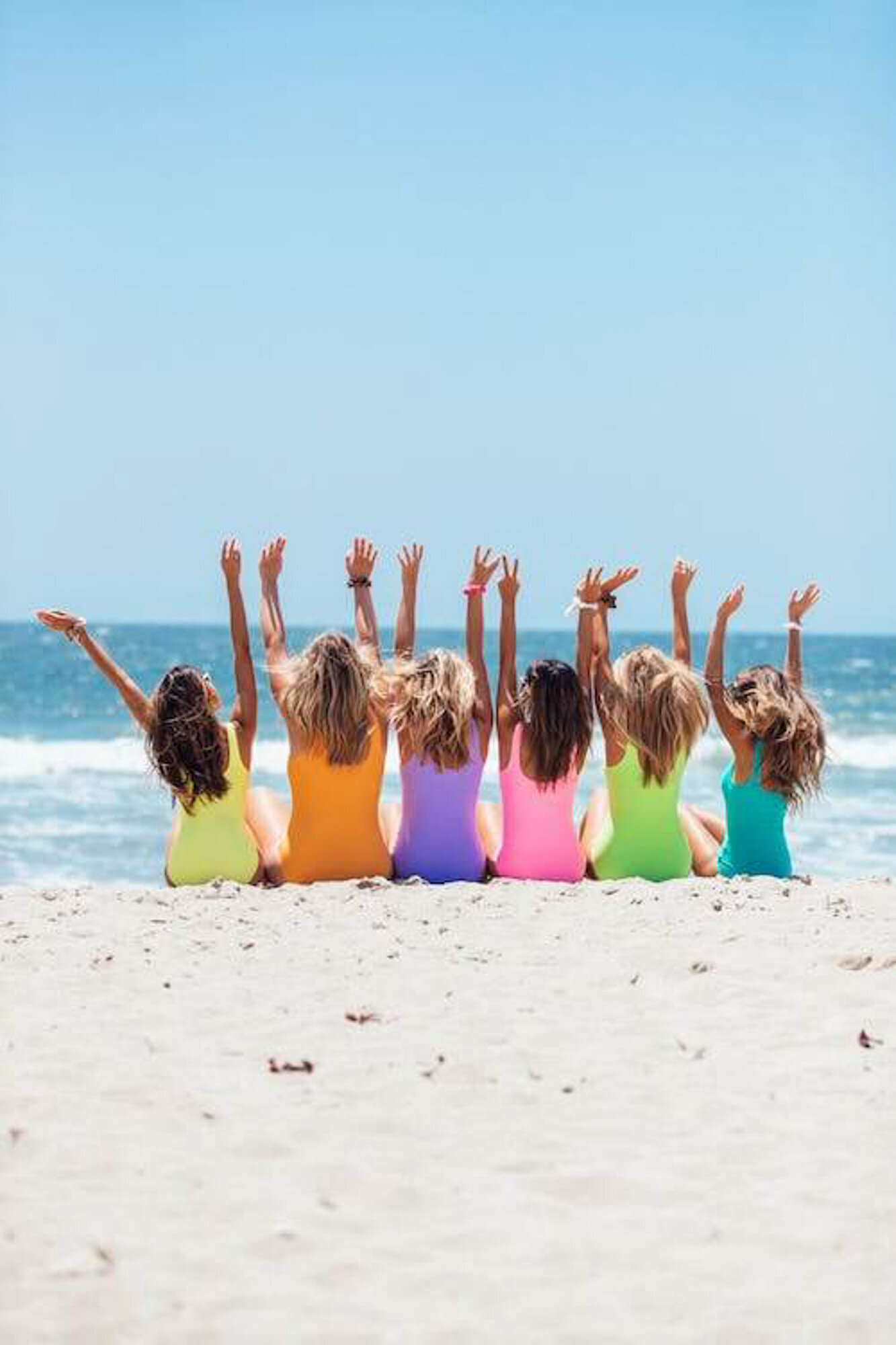 Group of friends taking photo wearing their colorful swimsuits by the seashore