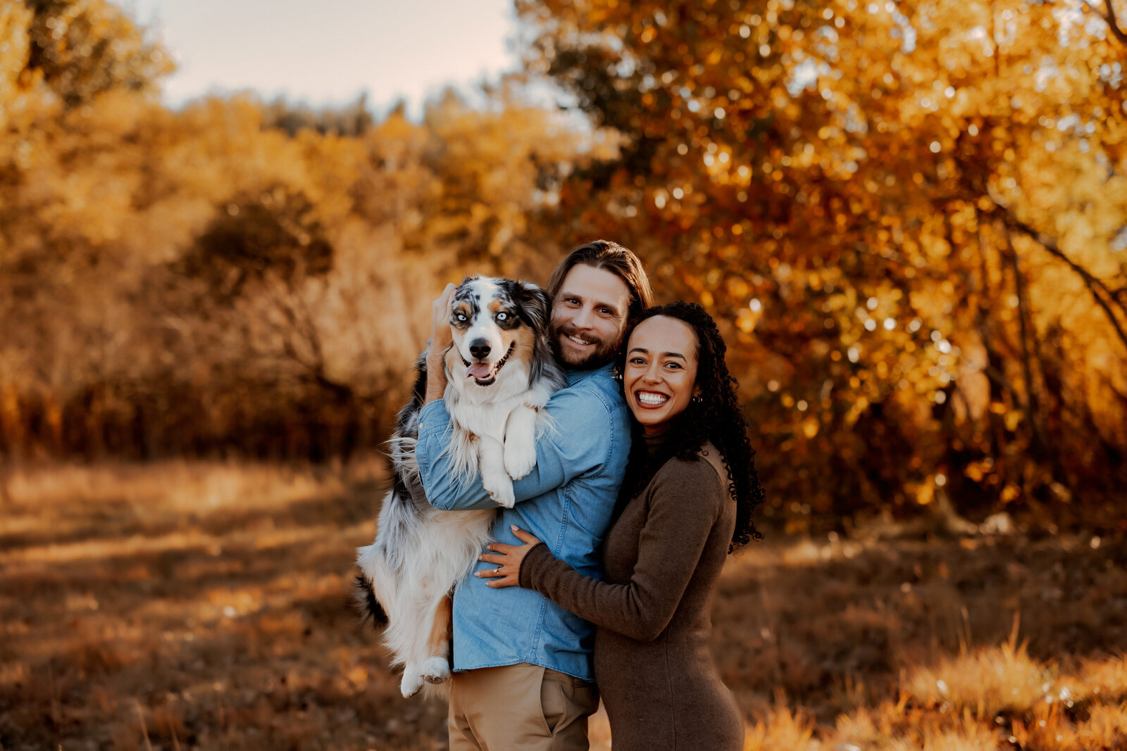 husband and wife hold dog for family pictures during fall for family photos