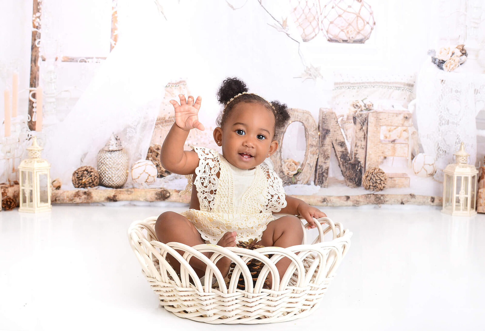 girl waves at camera while sitting in a rustic woven basket with a simple white one themed background